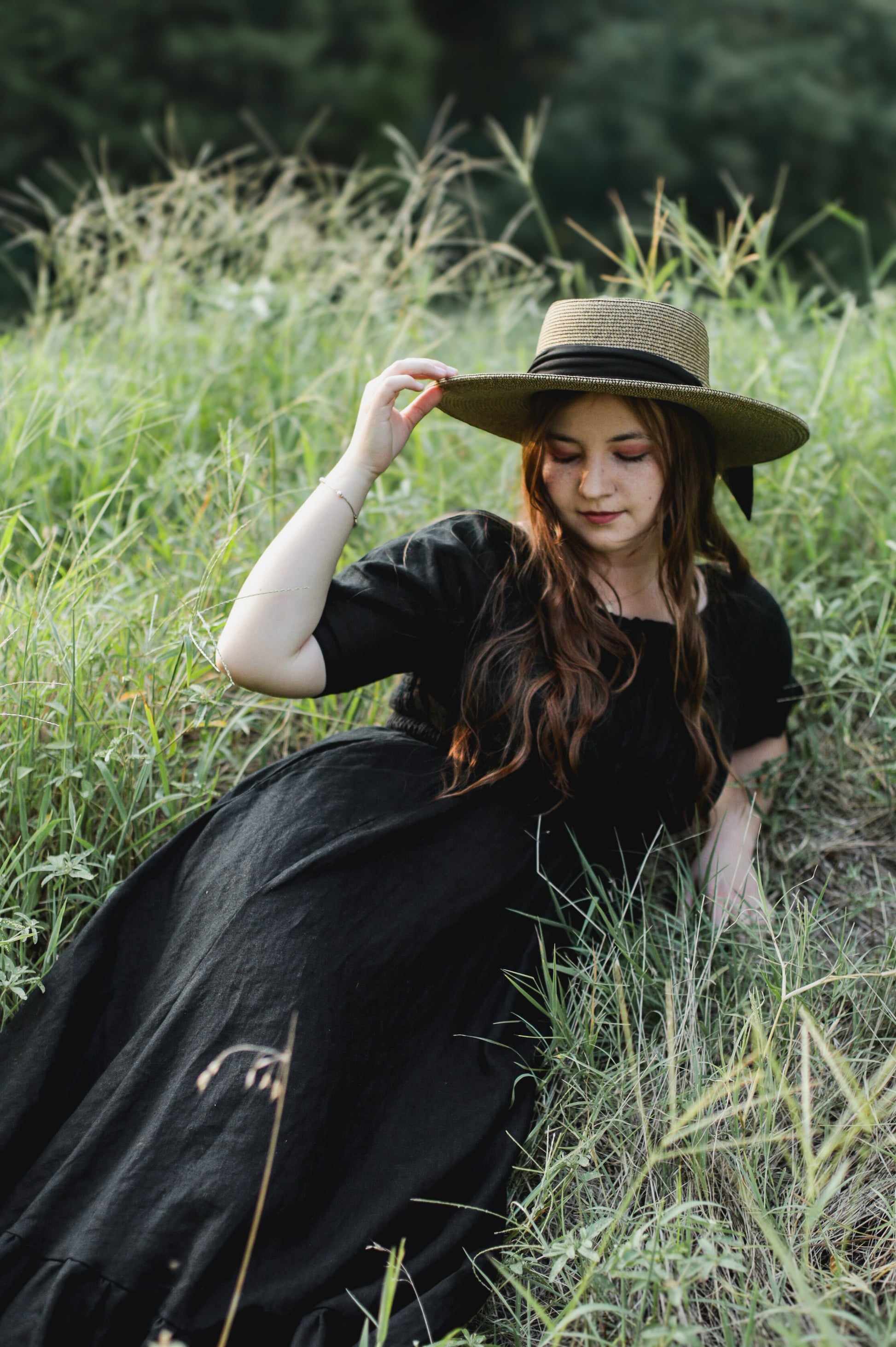 Woman in a black modest nursing dress and hat sitting in tall grass