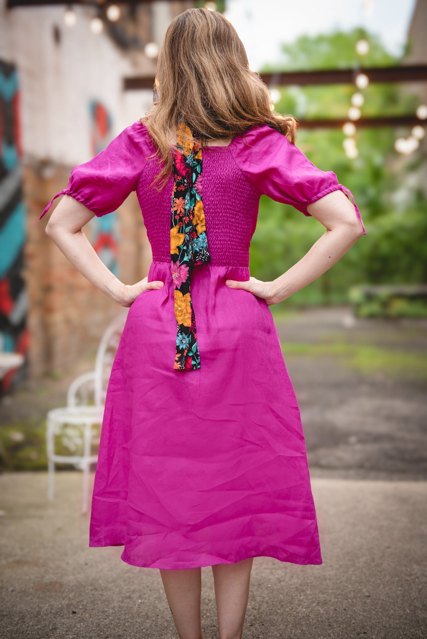 Woman wearing a bright pink modest nursing dress with a colorful scarf over her shoulder, standing outdoors.