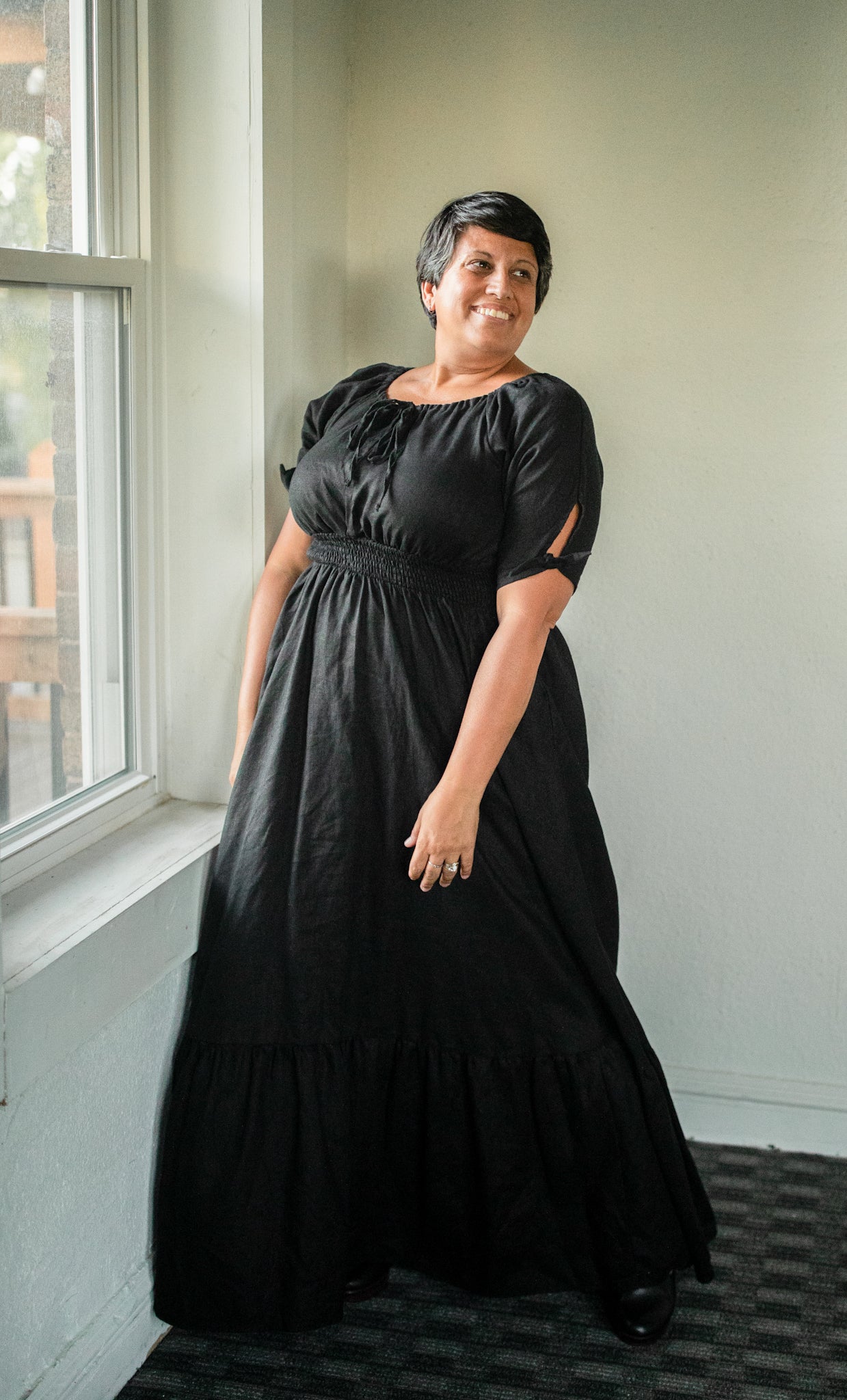 Woman wearing a black modest nursing dress standing by a window indoors.