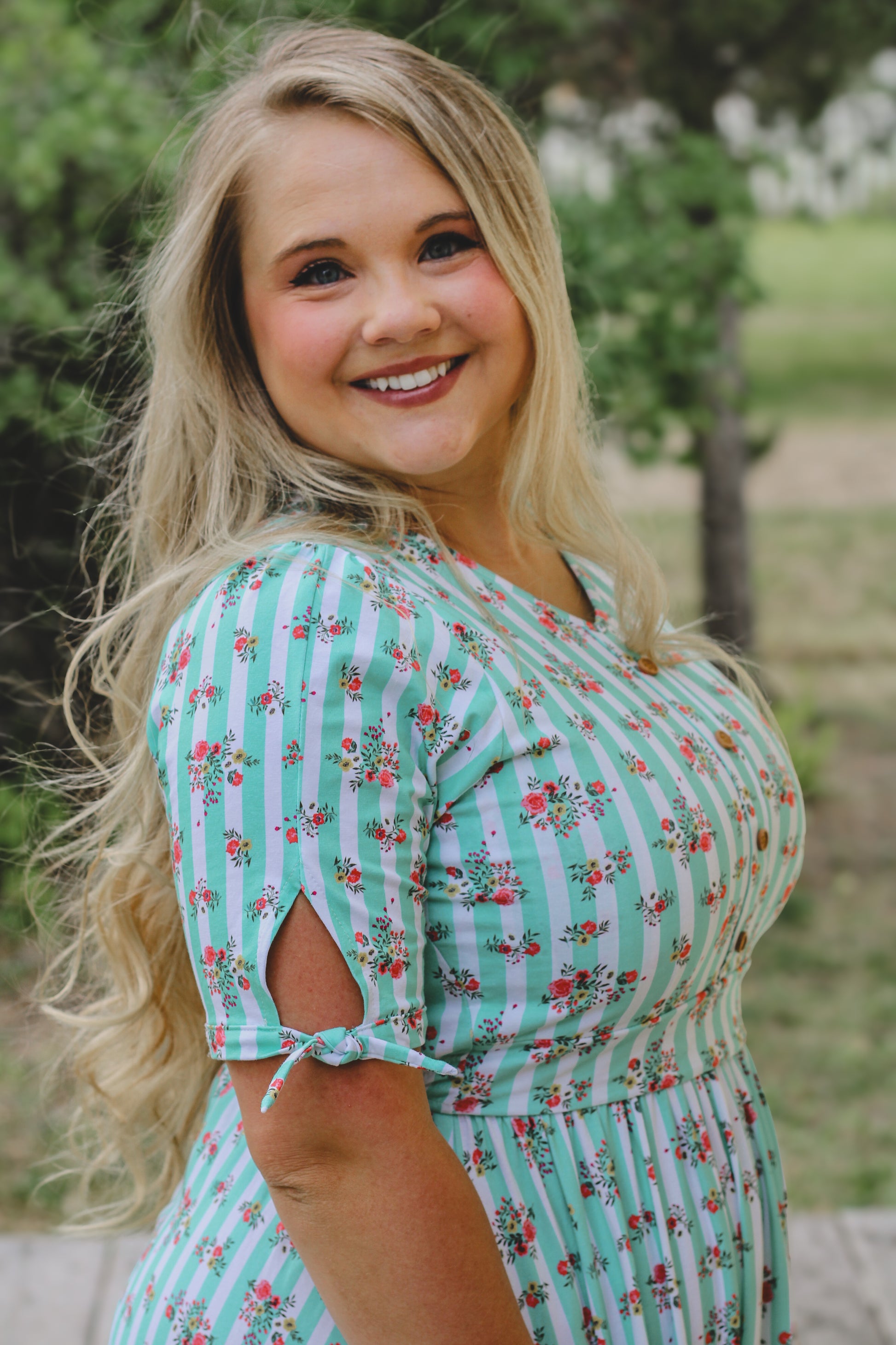 Woman wearing a green floral modest nursing dress standing outdoors with trees in the background