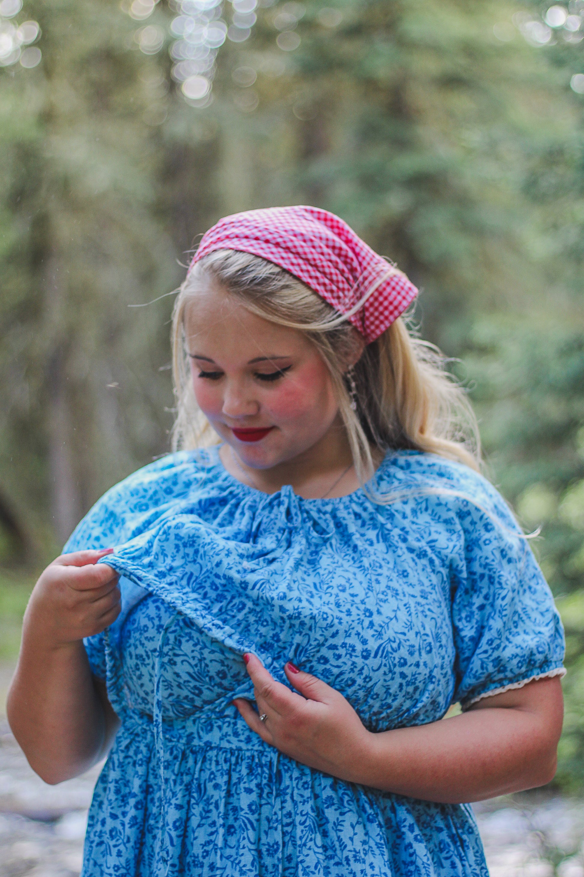 Woman wearing a blue modest nursing dress and pink headscarf in a forest setting