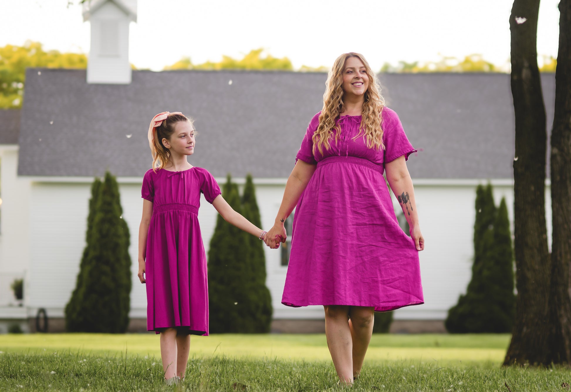 Mother and daughter in matching pink modest dresses walking outdoors on a grassy area.