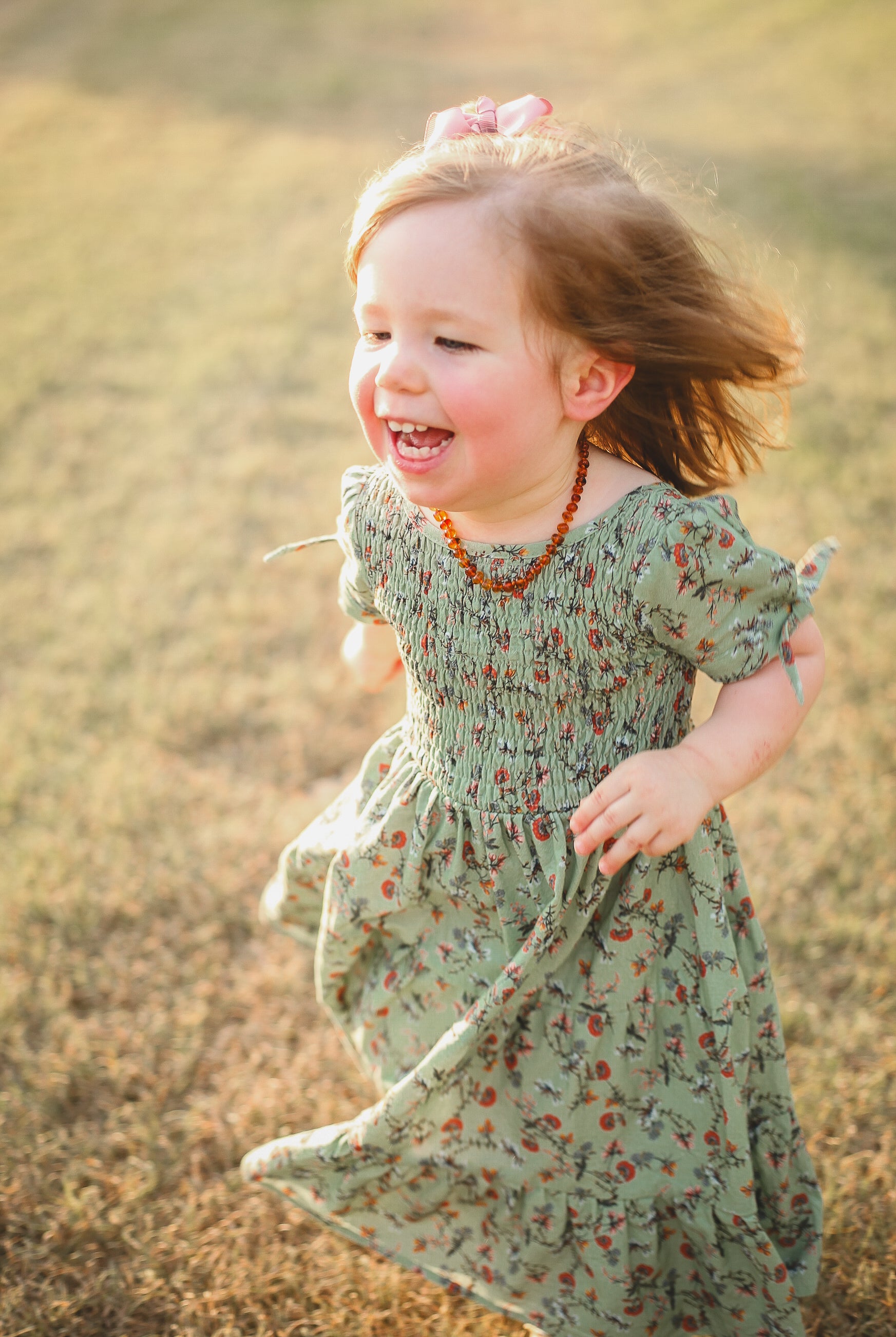 Child in a floral dress running in a field with sunlight
