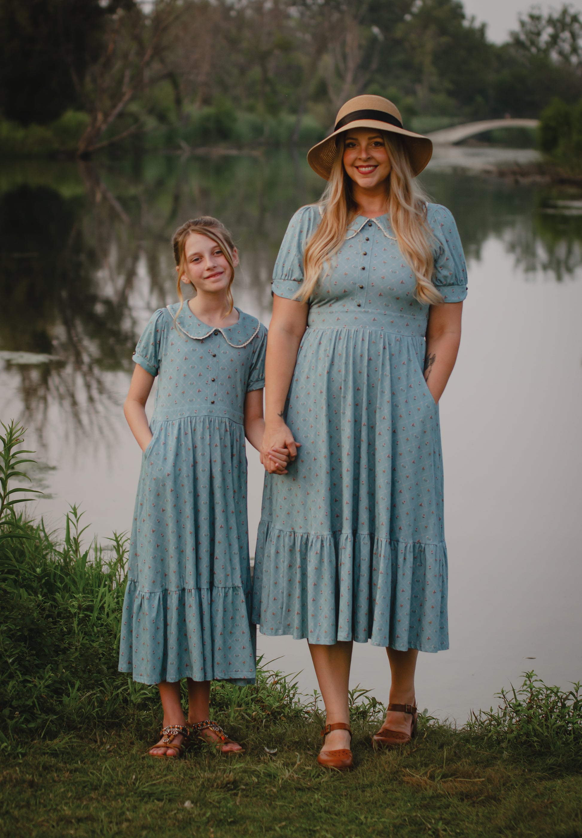 Mother and daughter in matching modest dresses standing by a lake.
