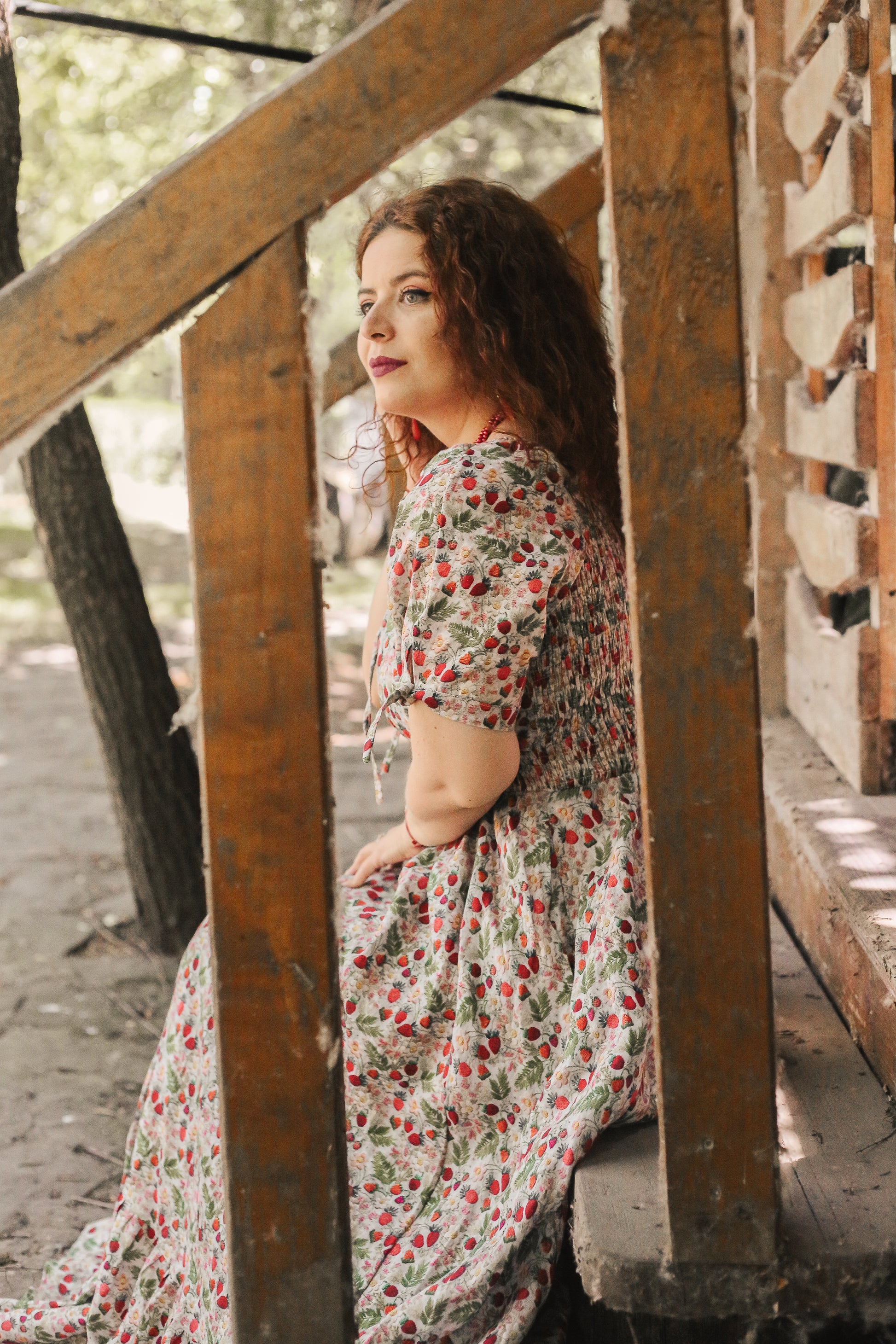 Woman in a floral modest nursing dress standing near wooden beams outdoors