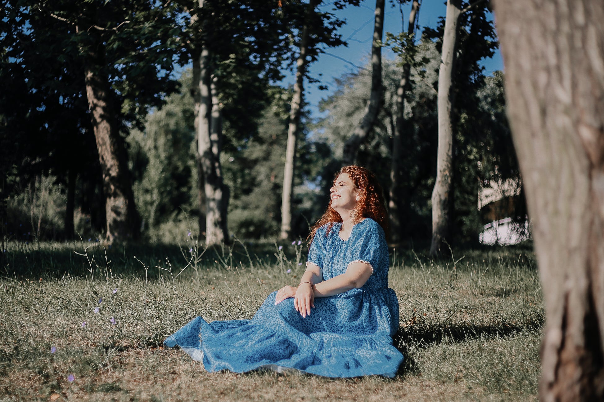 Woman in a blue modest nursing dress sitting under a tree in a park