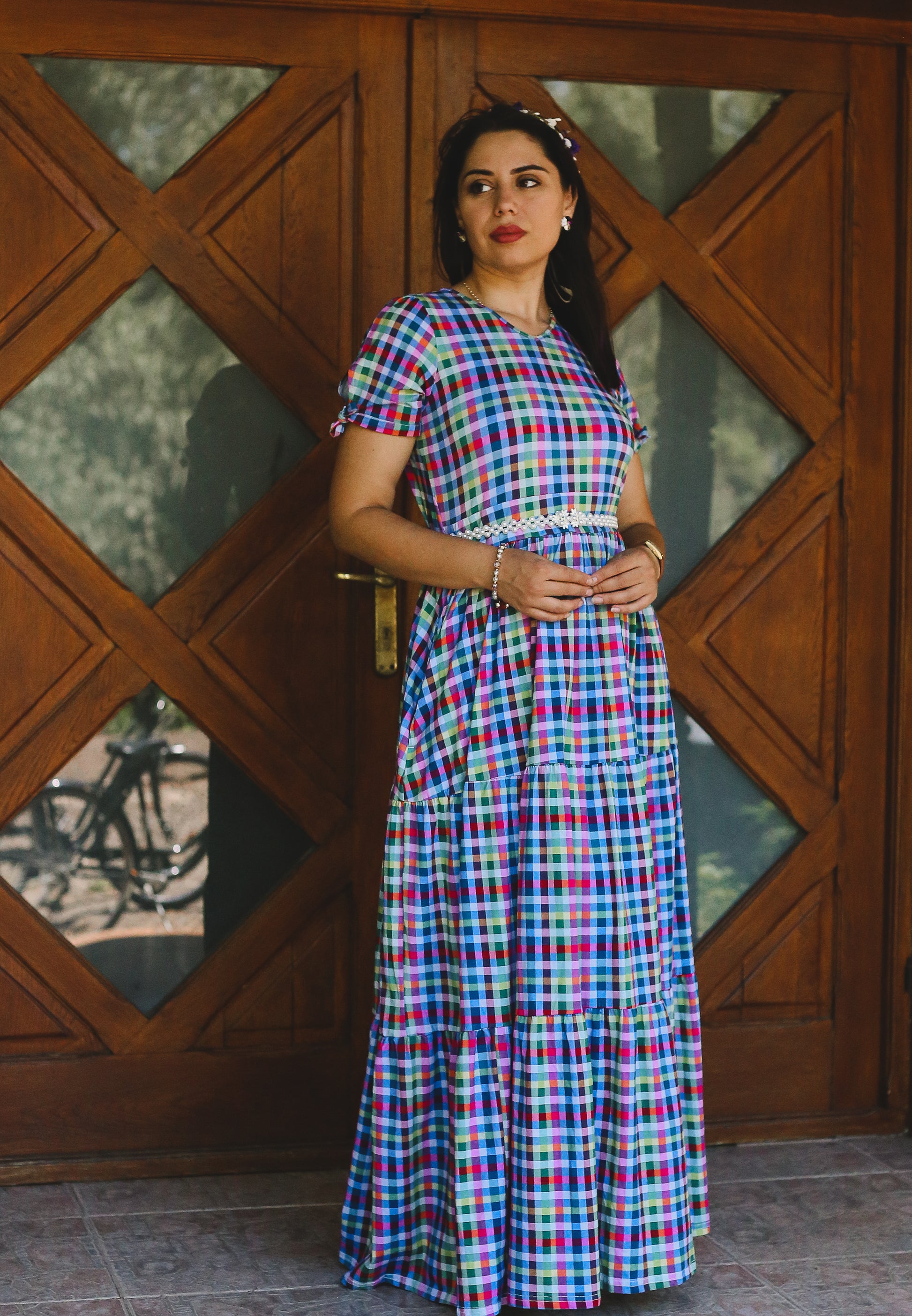 Woman wearing a colorful checkered modest nursing dress standing in front of a wooden door.