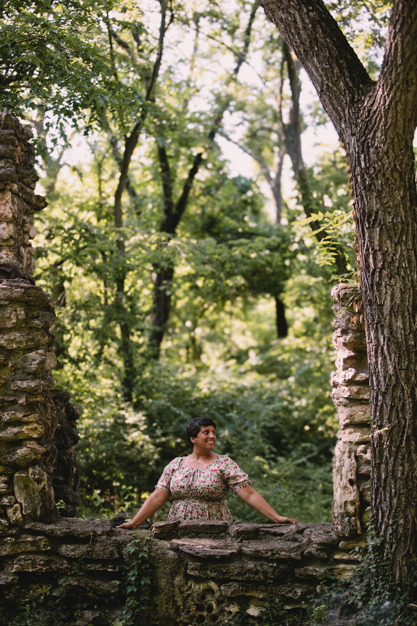 Woman sitting on stone ruins in a forest wearing a modest nursing dress
