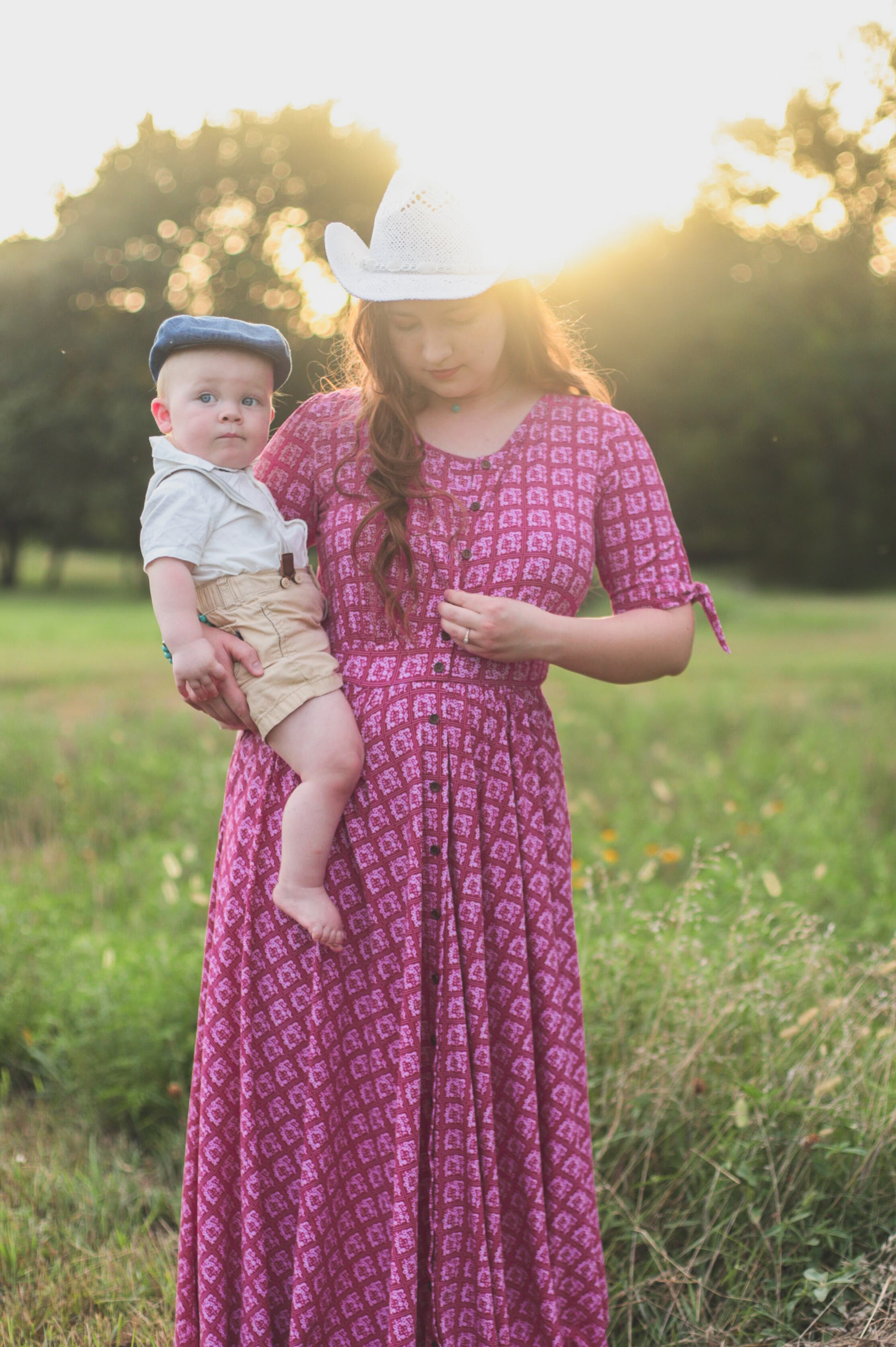 Woman in a pink modest nursing dress holding a baby in a field with a blurred background