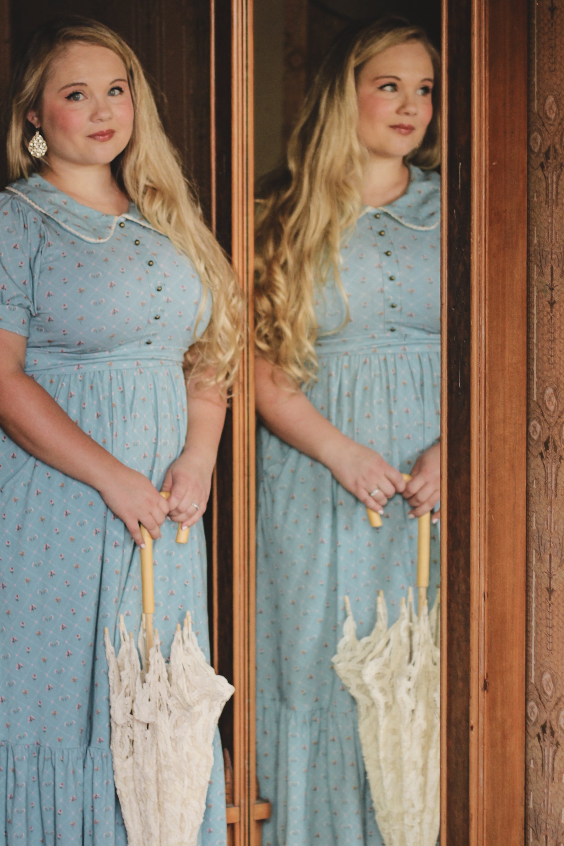 Woman in a blue modest nursing dress holding an umbrella, reflected in a wooden frame.