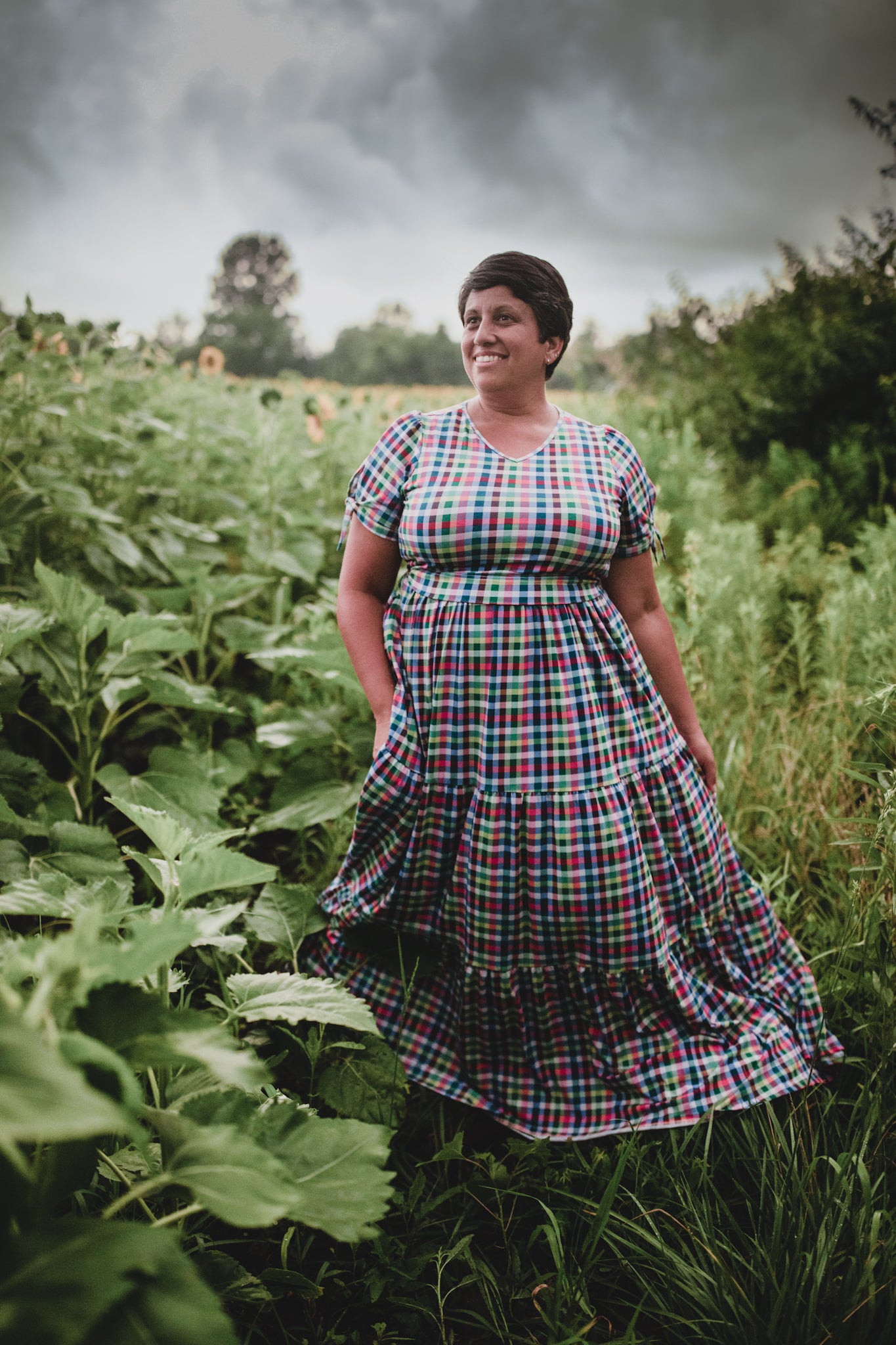 Woman in a plaid modest nursing dress standing in a field with a stormy sky.