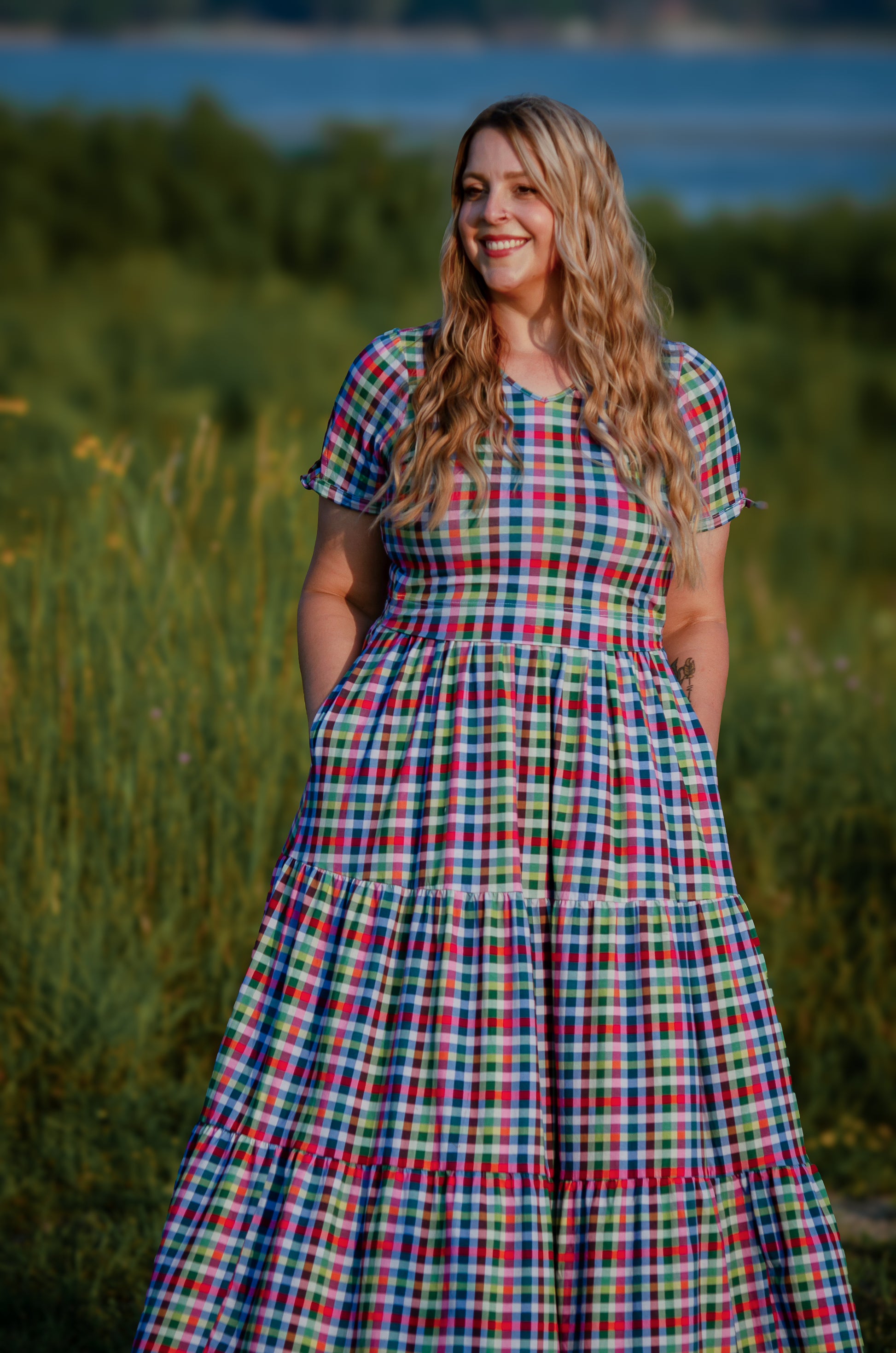 Woman in a plaid modest nursing dress standing in a field with a scenic background