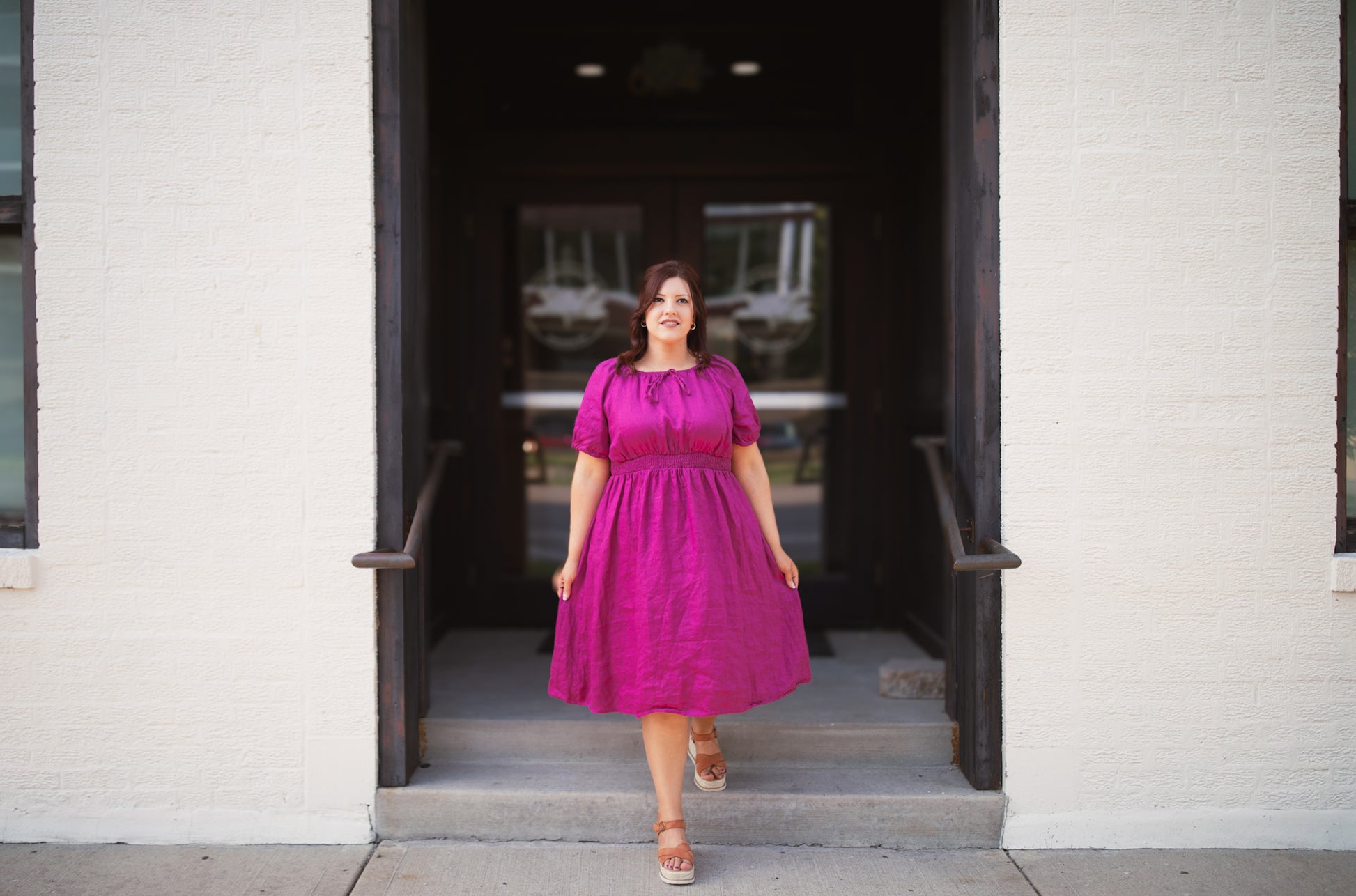 Woman in a pink modest nursing dress standing in front of a building entrance.