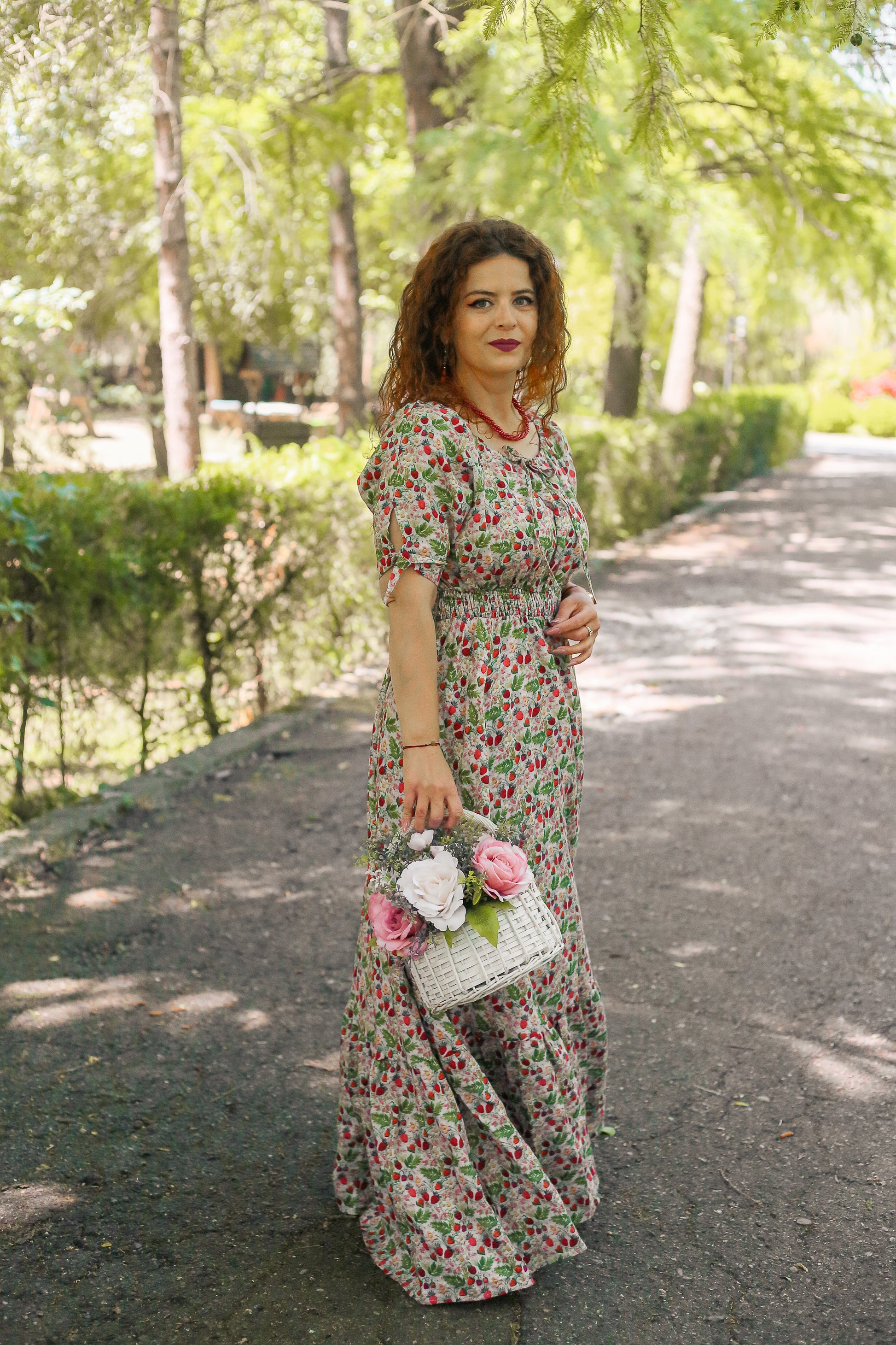 Woman in a floral modest nursing dress holding a floral handbag on a tree-lined street.