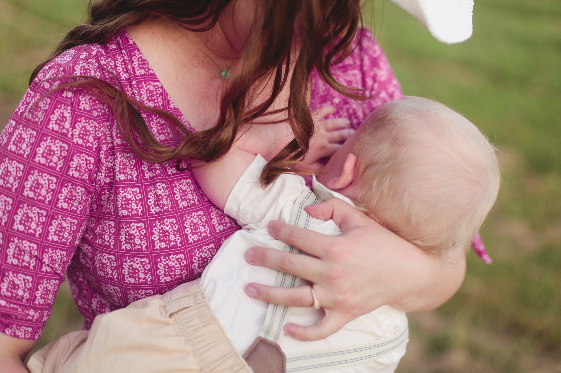 Woman in a pink patterned modest nursing dress holding a baby outdoors.
