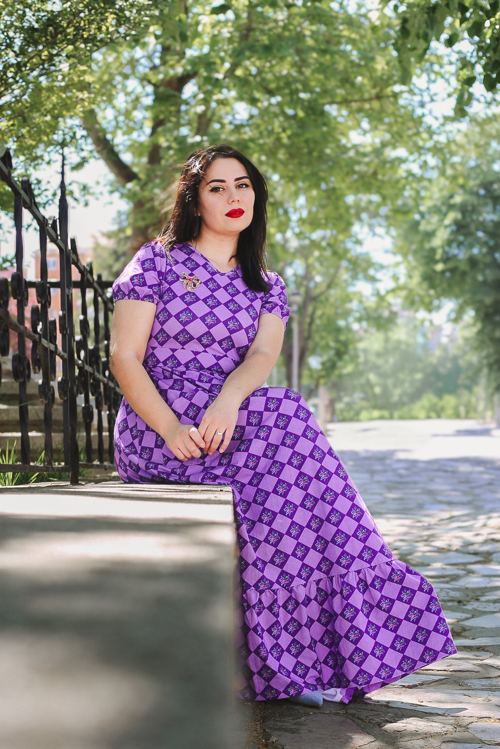 Woman in a purple checkered modest nursing dress sitting outdoors.