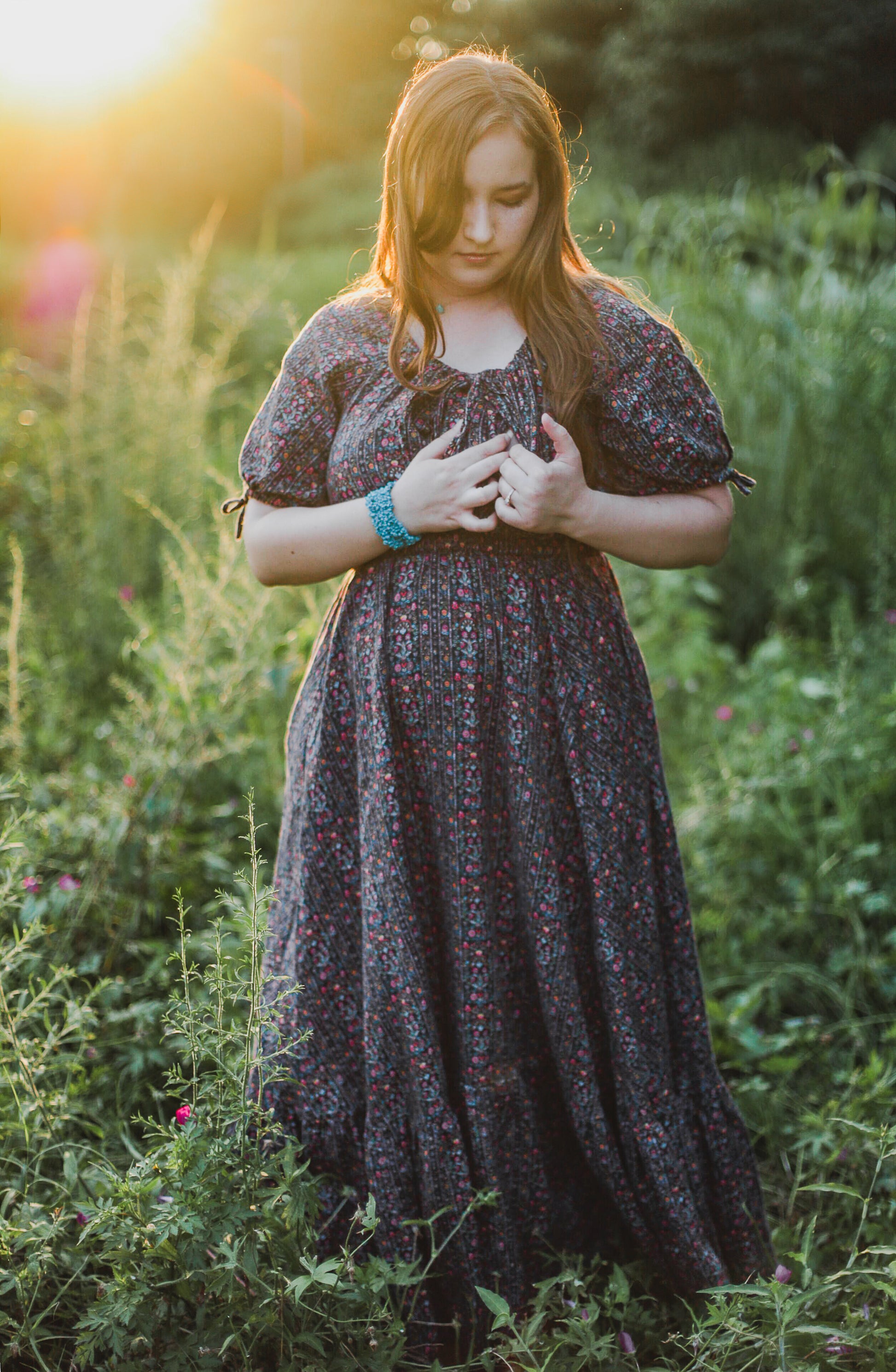 Woman in a floral modest nursing dress standing in a field with a warm glow