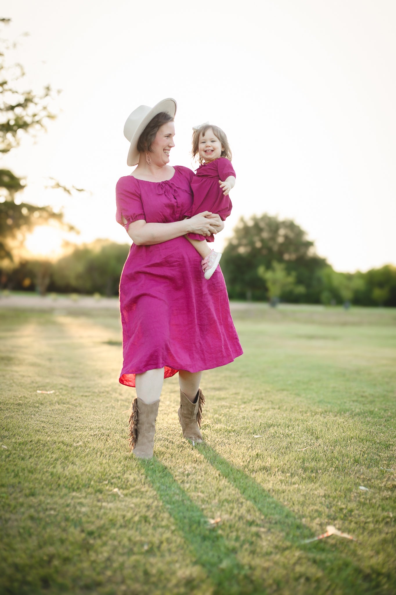 Woman in a pink modest nursing dress holding a child in a park at sunset