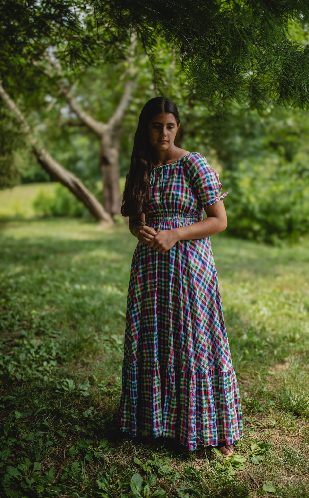 Woman in a colorful modest nursing dress standing in a grassy area with trees in the background