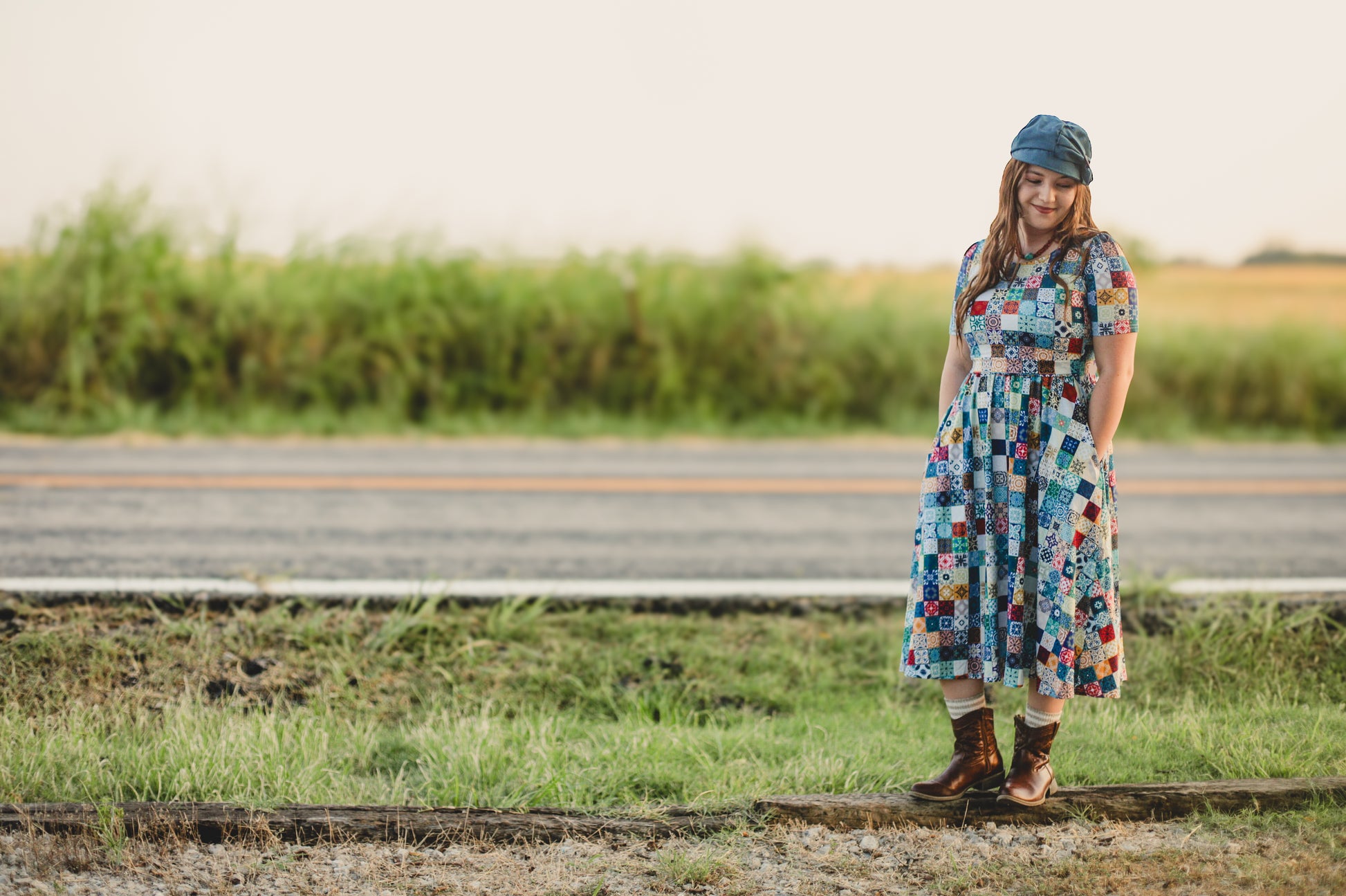 Woman in a colorful modest nursing dress standing on a road with a field in the background