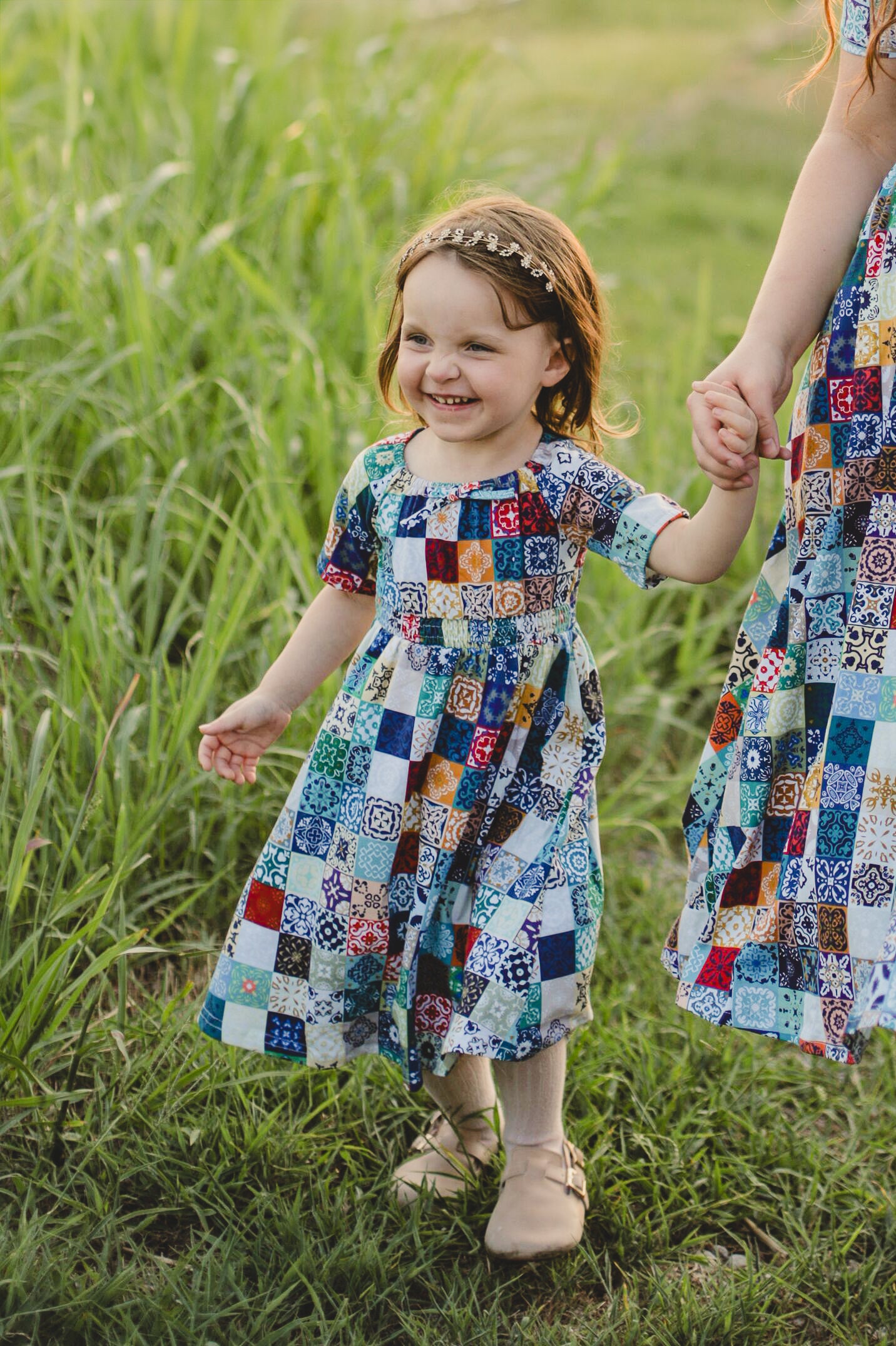 Child in colorful patchwork dress standing in a grassy field