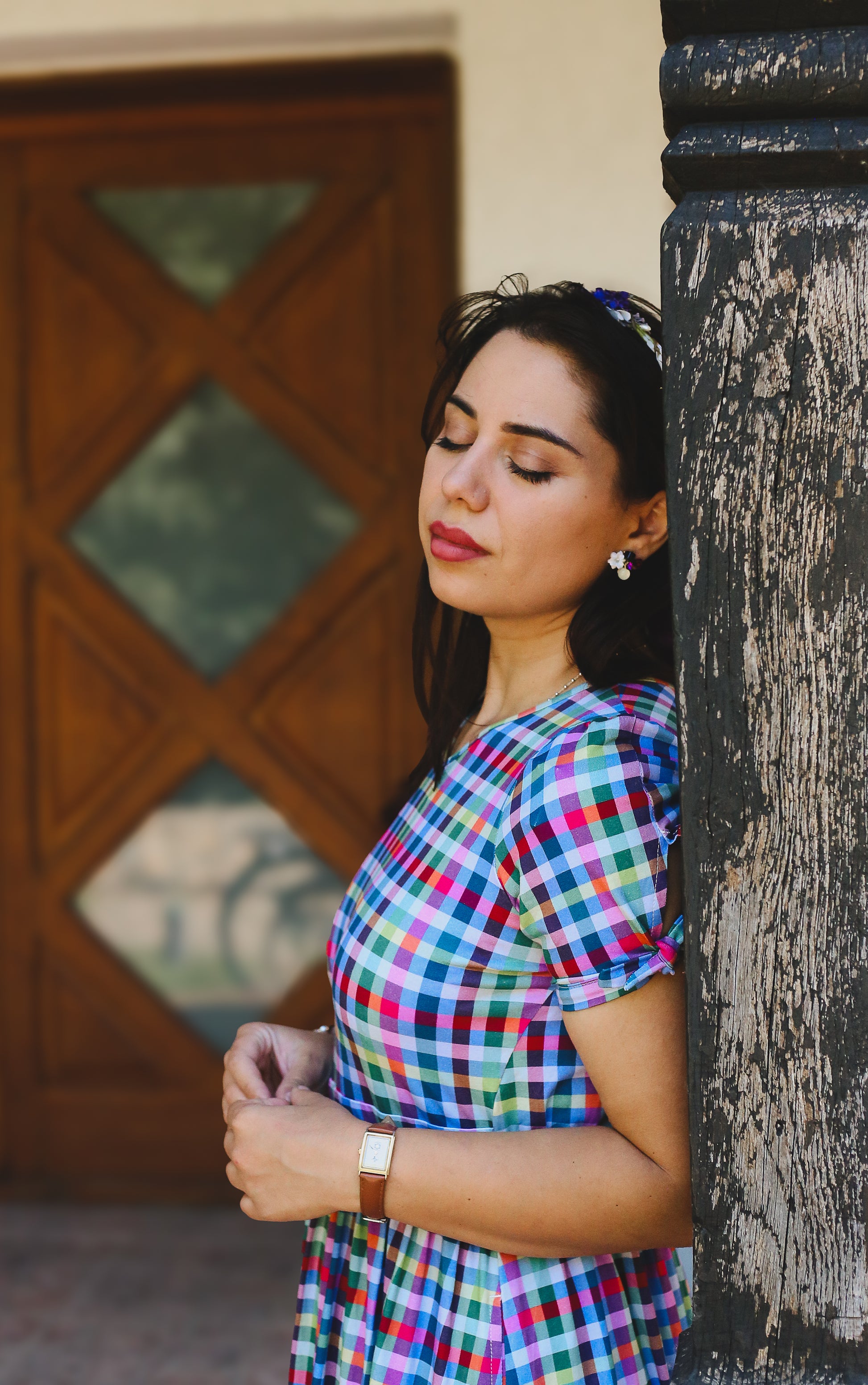 Woman in a colorful checkered modest nursing dress standing against a textured wall.