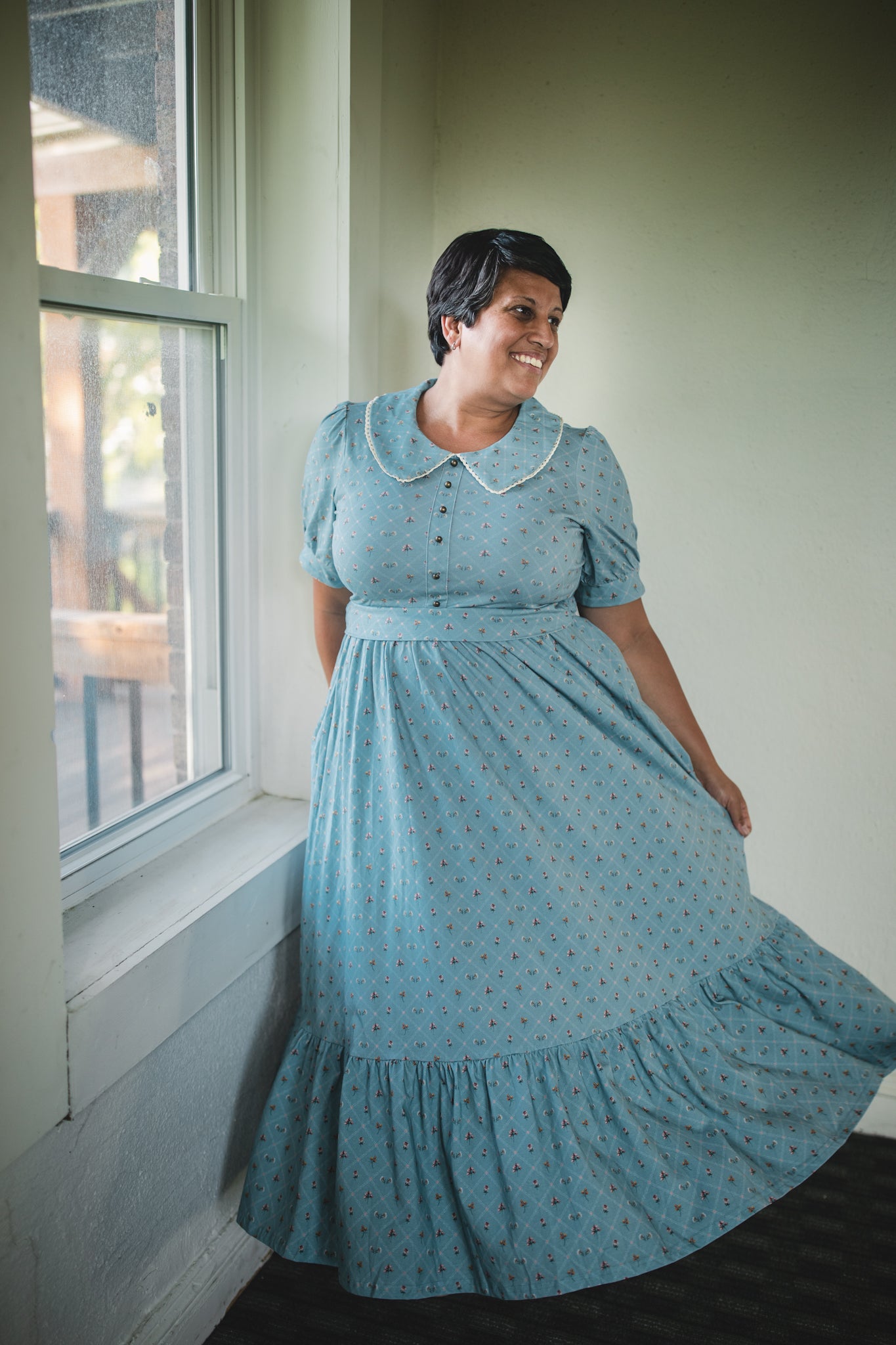Woman wearing a blue vintage modest nursing dress standing by a window.