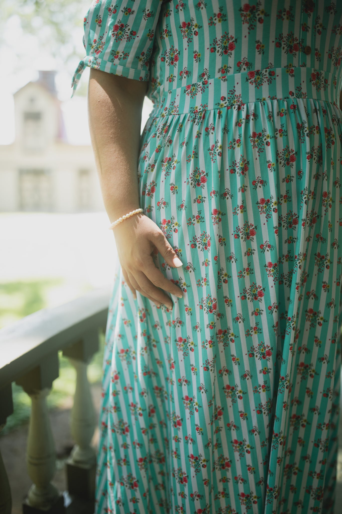 Person wearing a green modest nursing dress with floral pattern and stripes, standing outdoors.