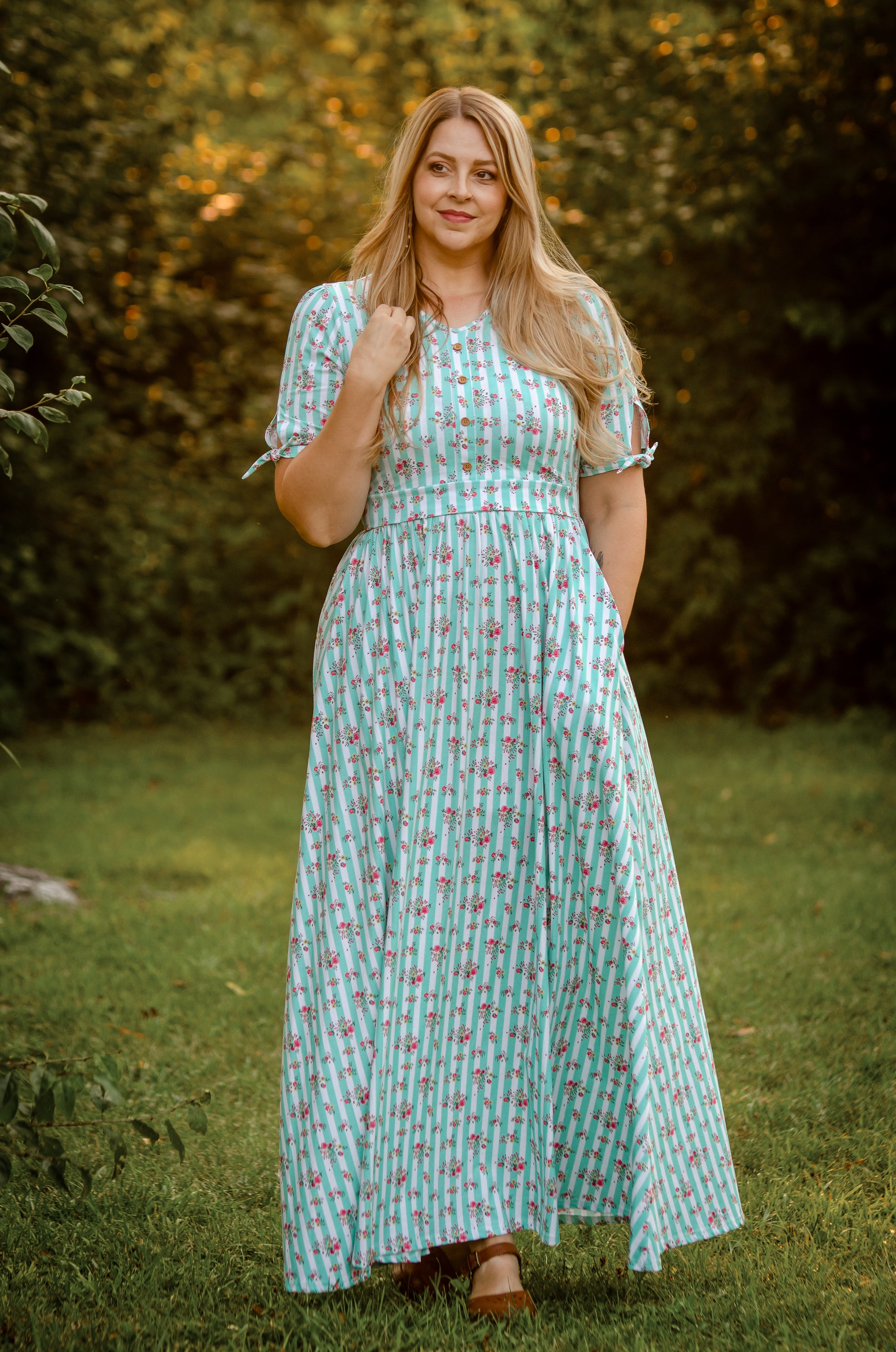 Woman in a green patterned modest dress standing outdoors with trees in the background