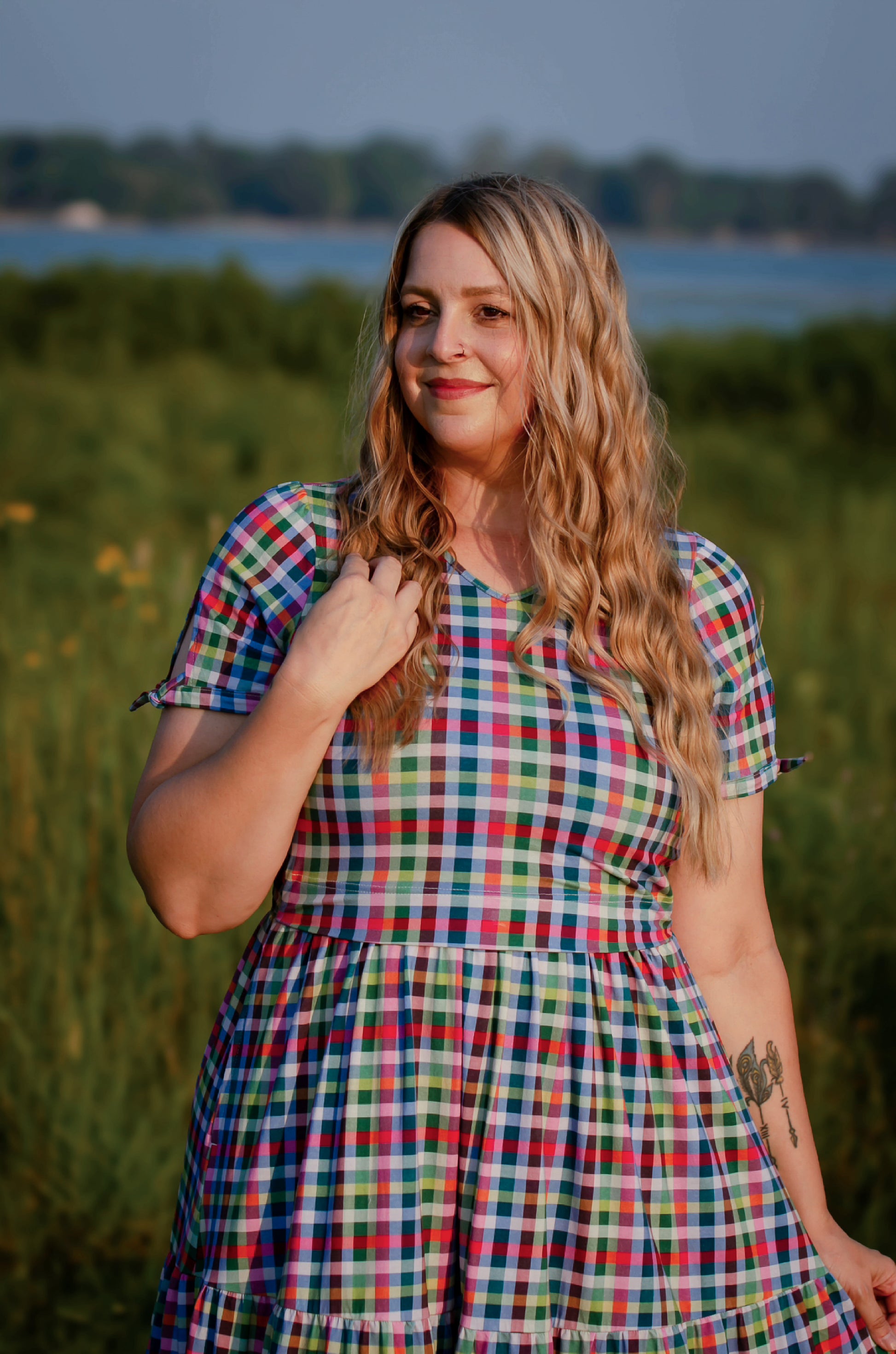 Woman in a colorful checkered modest nursing dress standing in a field with a blurred background