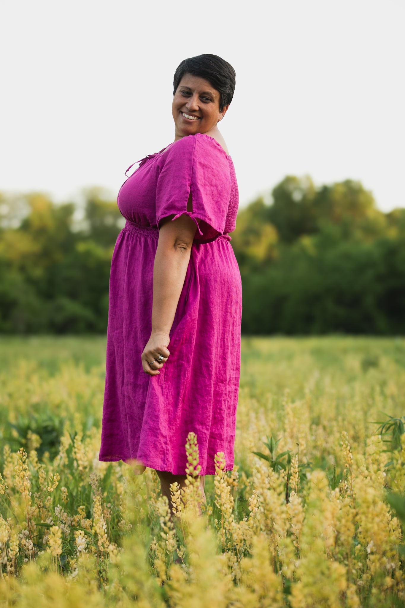 Woman in a pink modest nursing dress standing in a field with greenery in the background