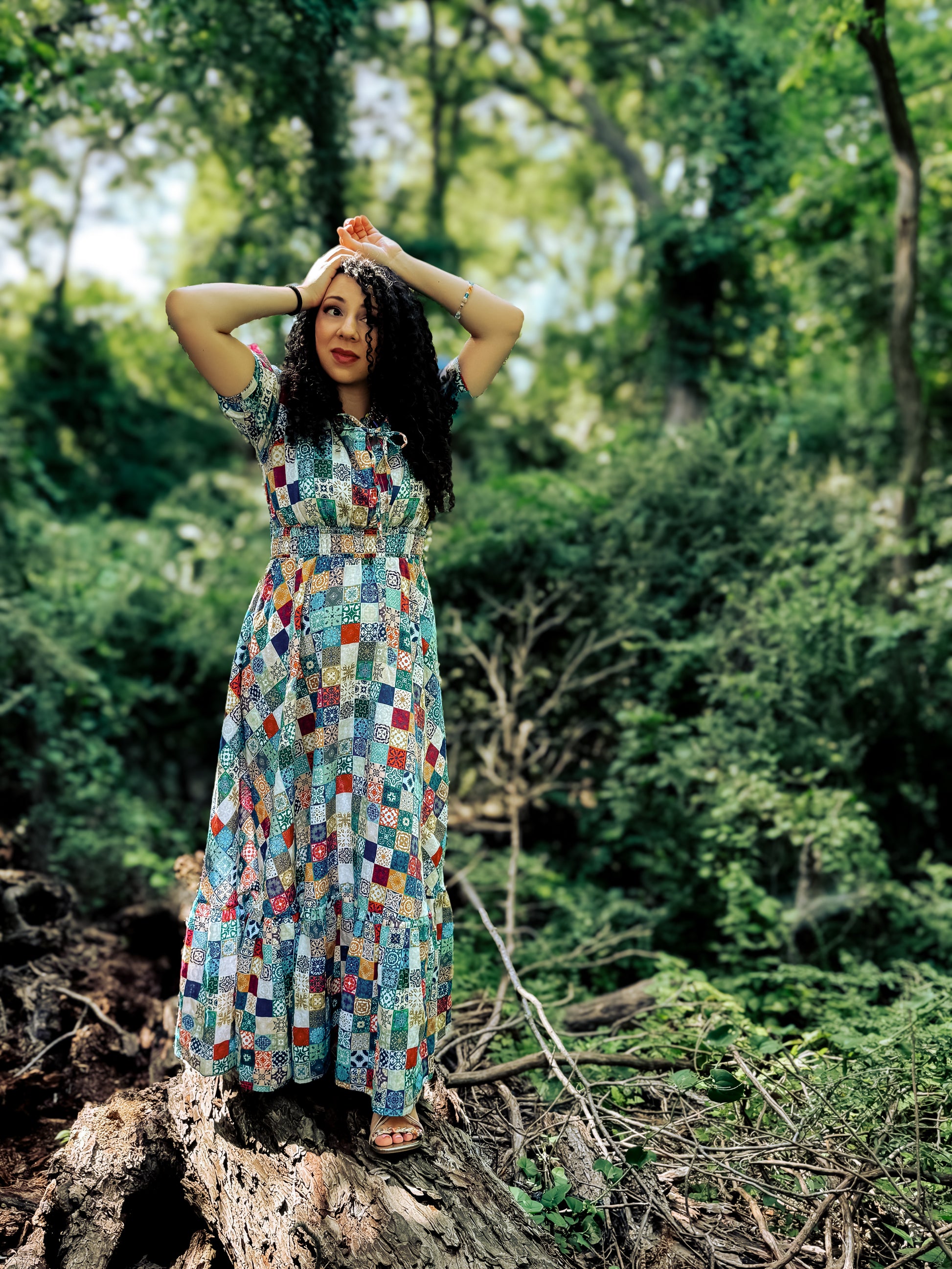 Woman in a colorful modest nursing dress standing on a log in a forest