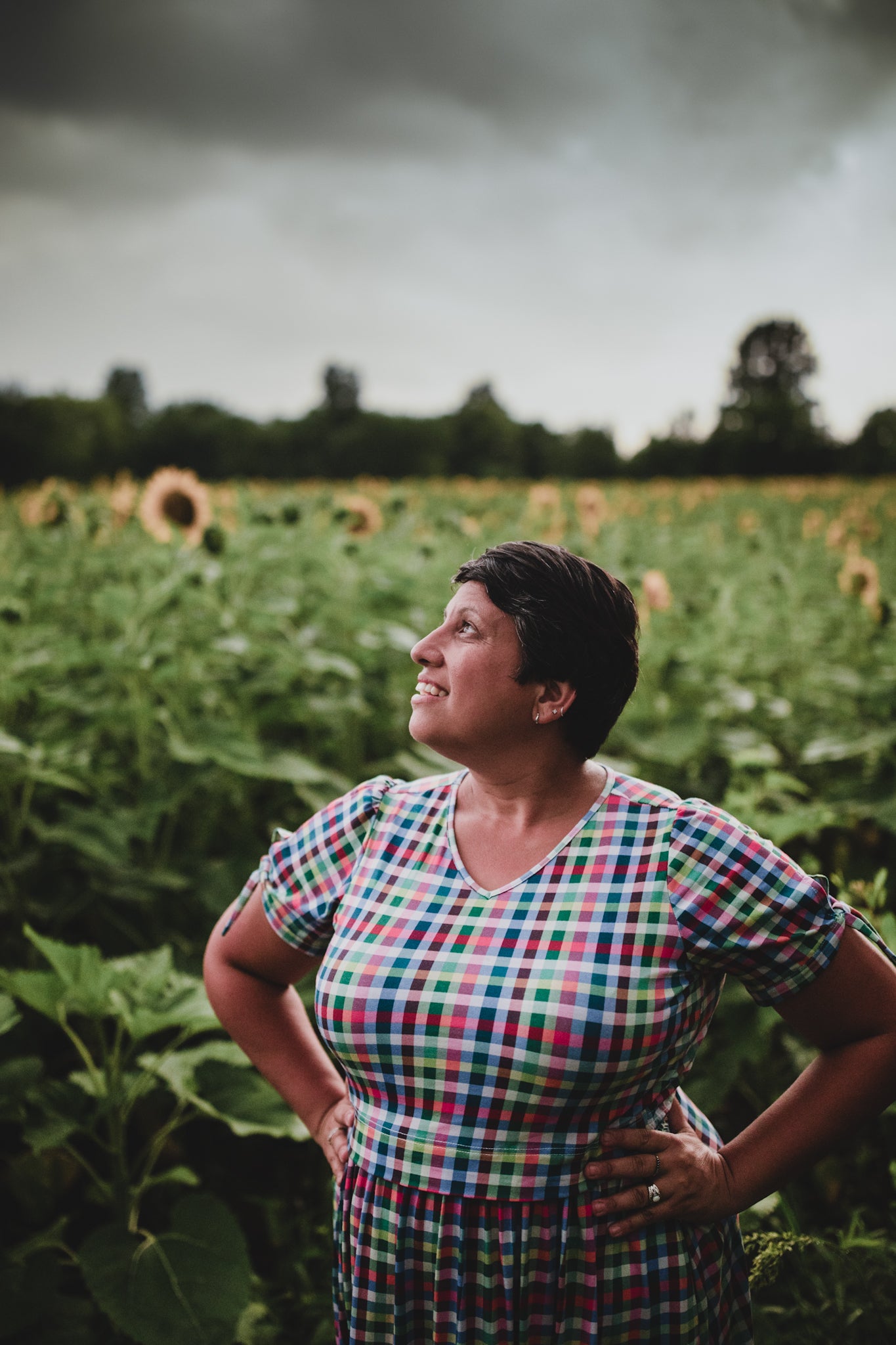 Woman standing in a sunflower field with a stormy sky wearing a modest nursing dress.
