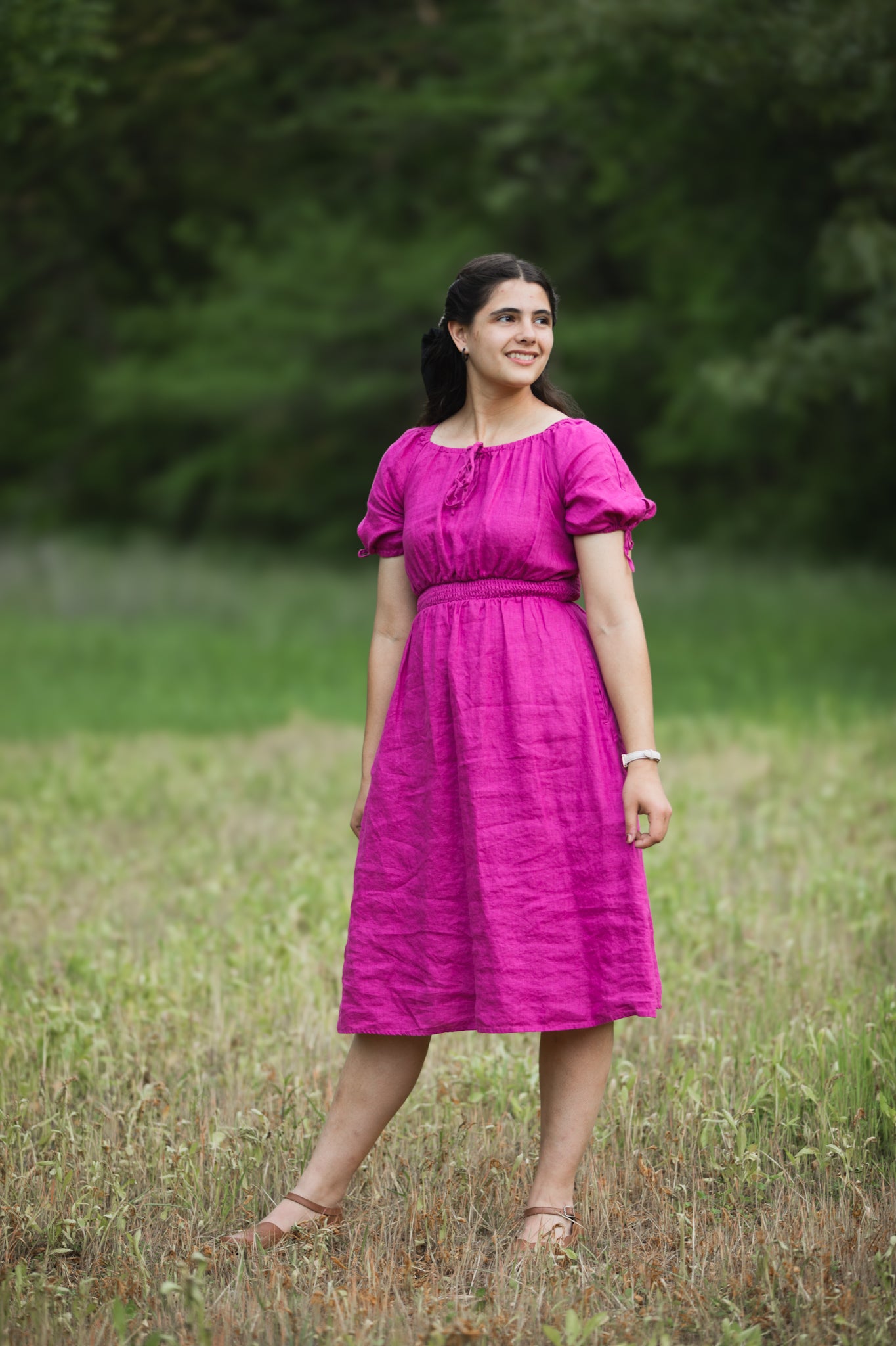 Woman in a pink modest nursing dress standing in a field with blurred green background