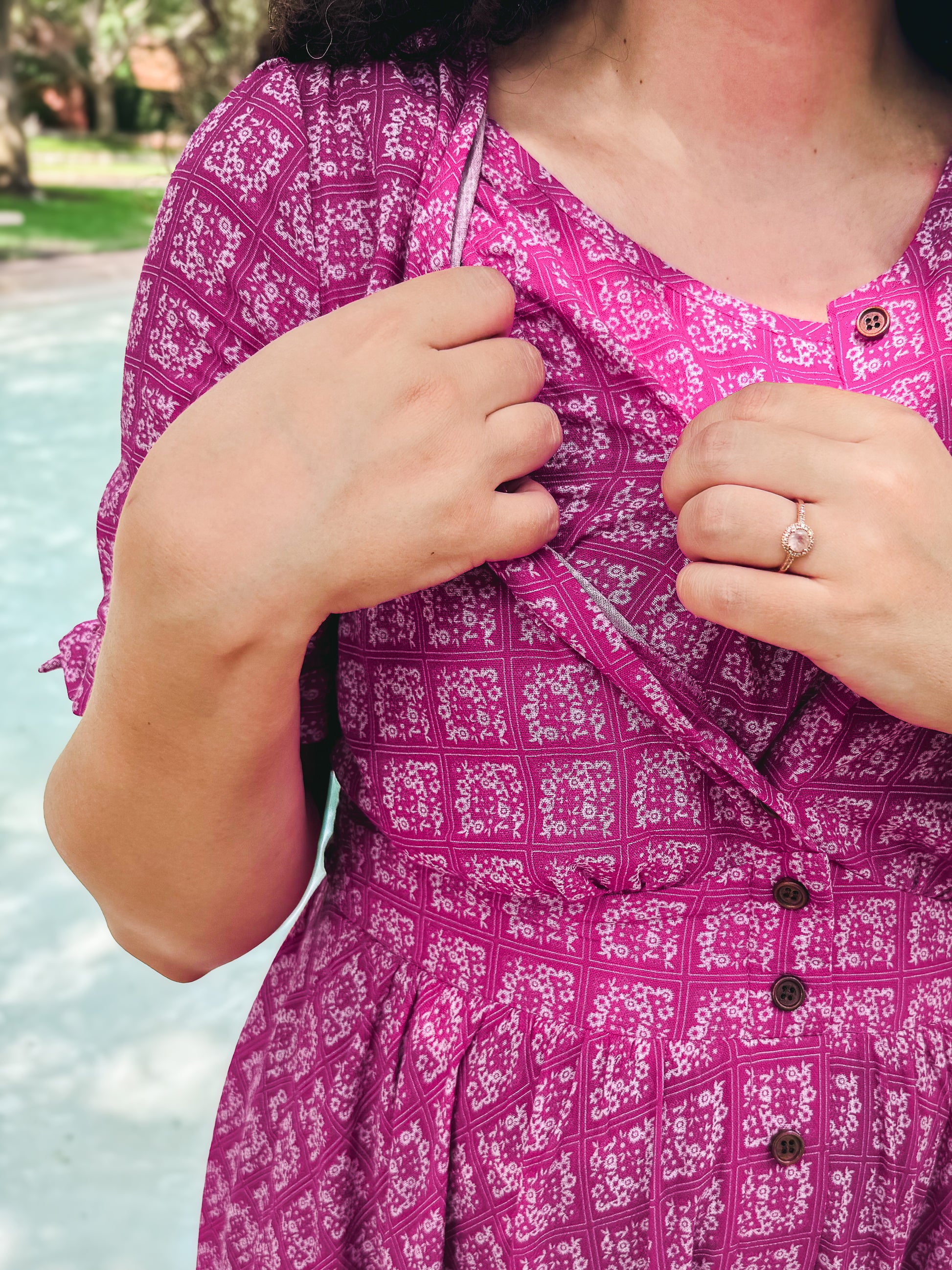 Person wearing a pink patterned modest nursing dress with buttons, standing by a pool.