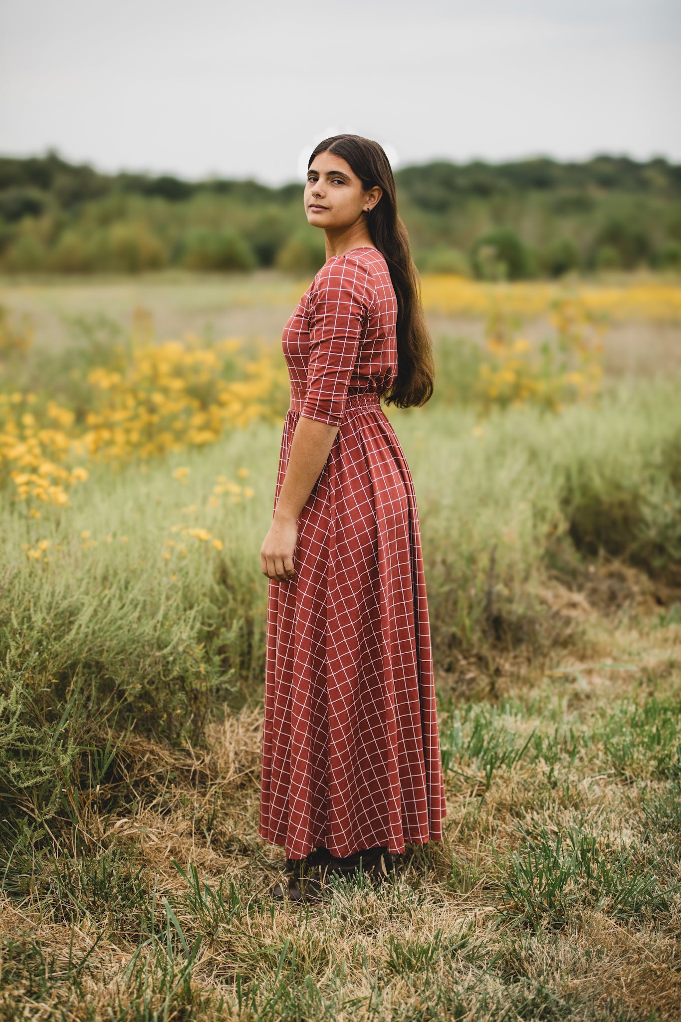 Woman in modest nursing copper windowpane dress wildflower field