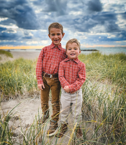 Two boys in matching red plaid shirts on beach