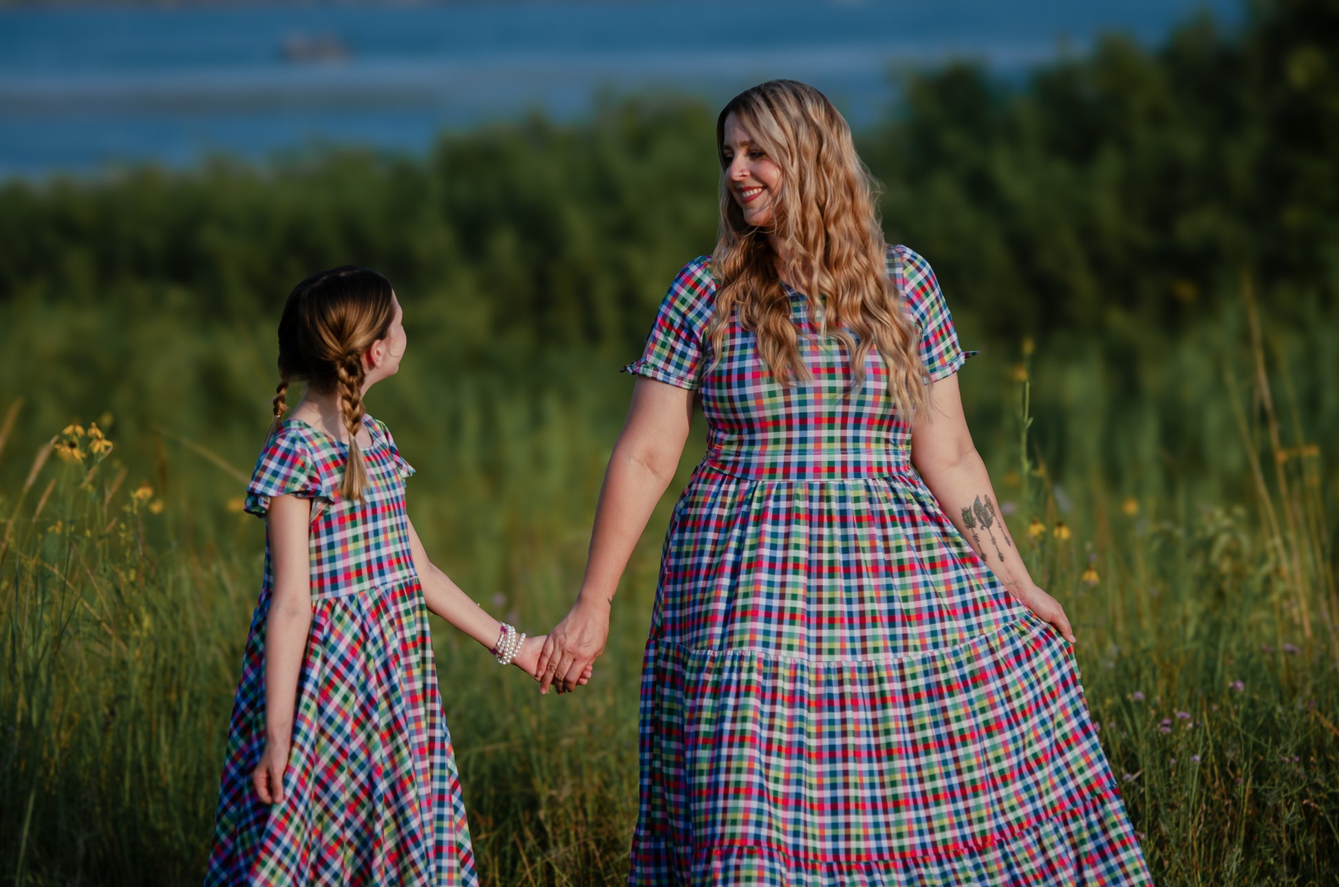 Woman and young girl holding hands in a field wearing matching plaid modest dresses.