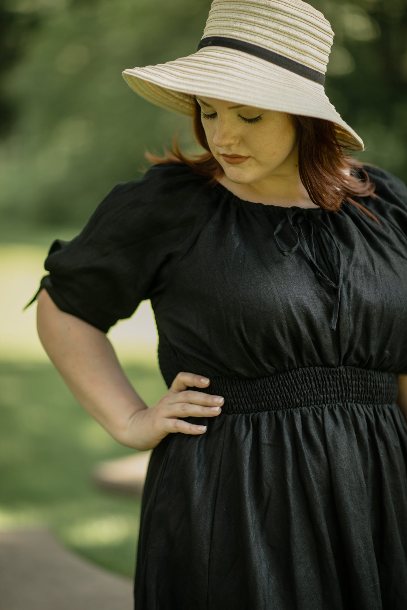 Woman wearing a black modest nursing dress and beige hat outdoors