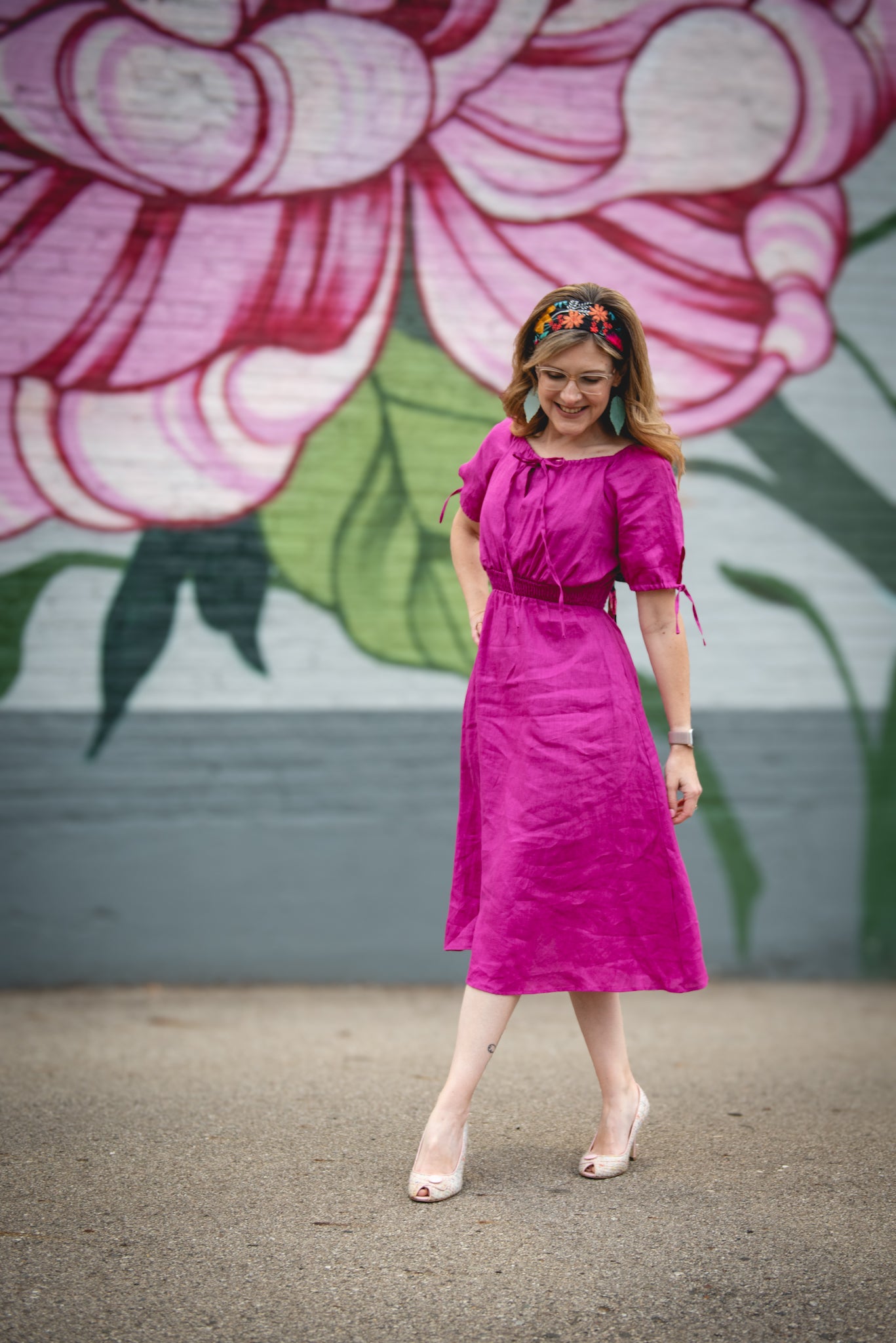 Woman in a bright pink modest nursing dress standing in front of a floral mural.