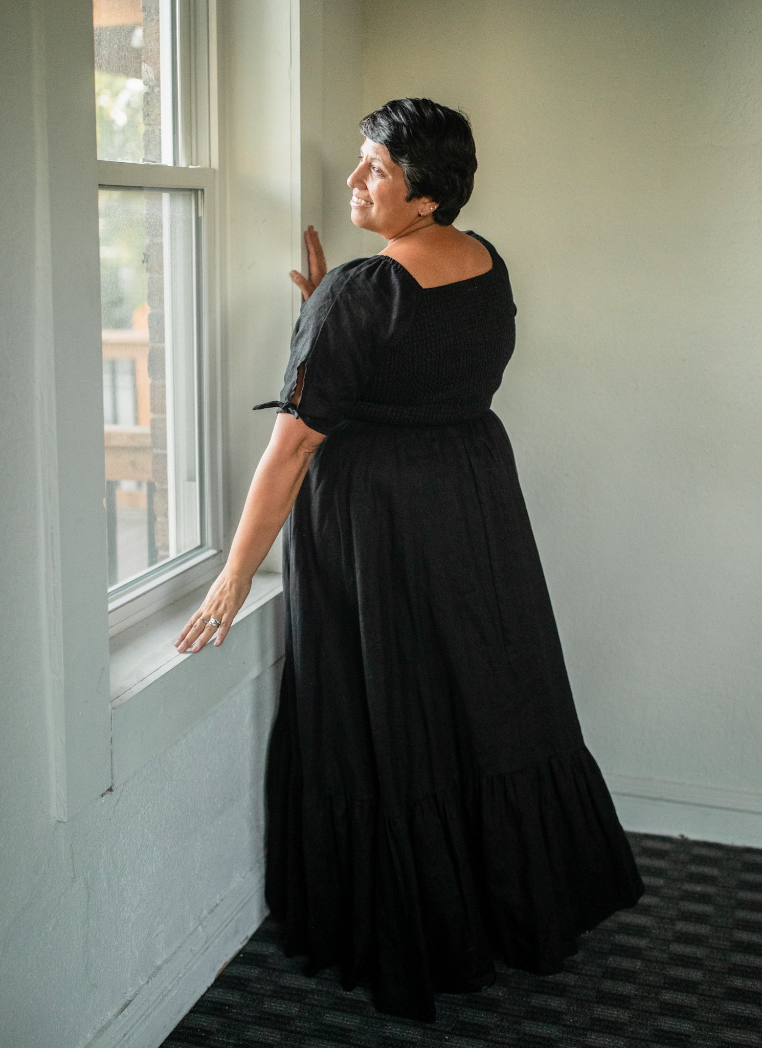 Woman in a black modest nursing dress standing by a window in a room with white walls.