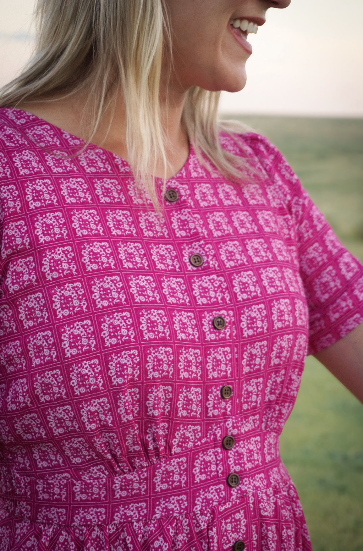 Person wearing a pink patterned modest nursing dress with buttons in an outdoor setting