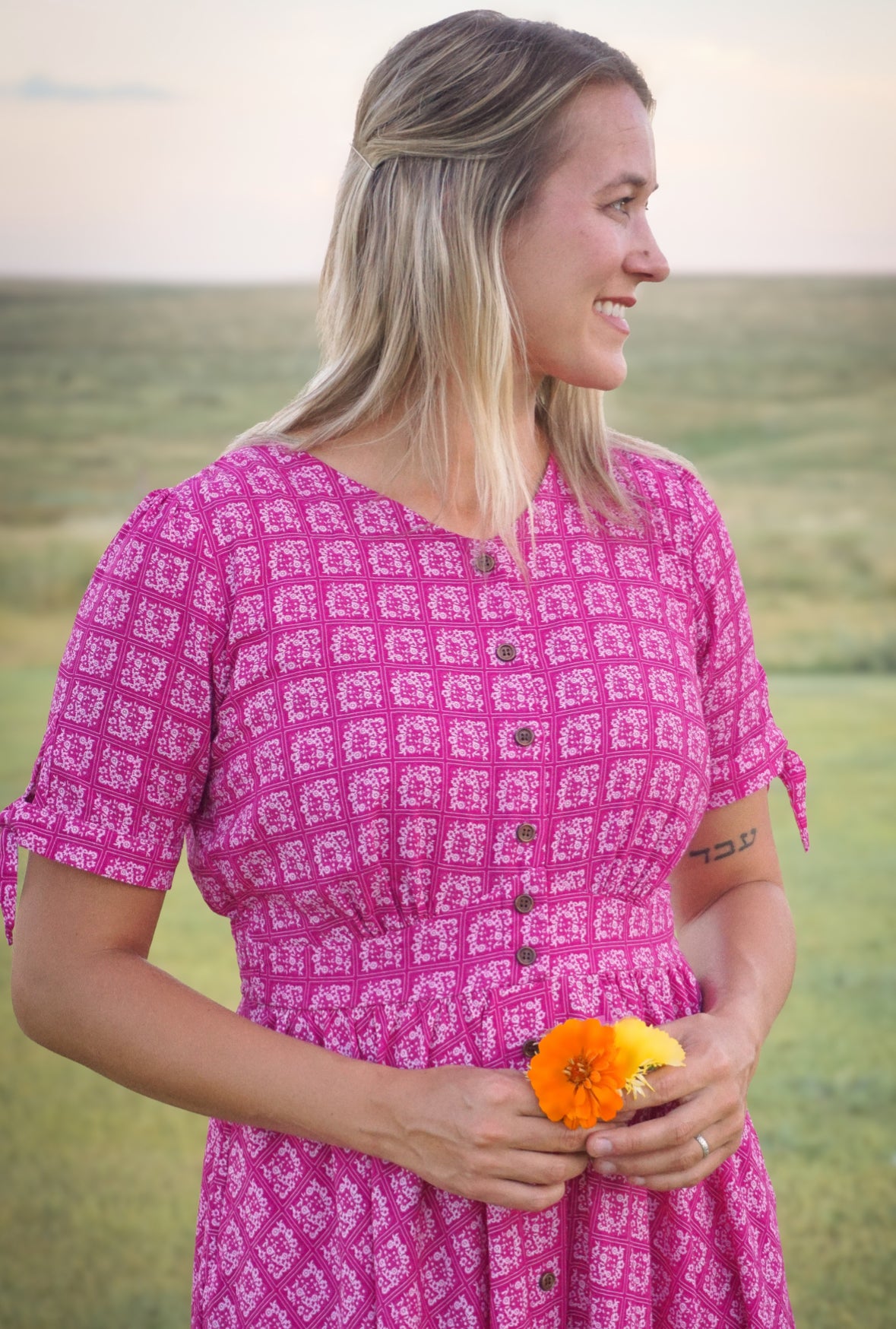 Woman in a pink patterned modest nursing dress holding a flower in a field