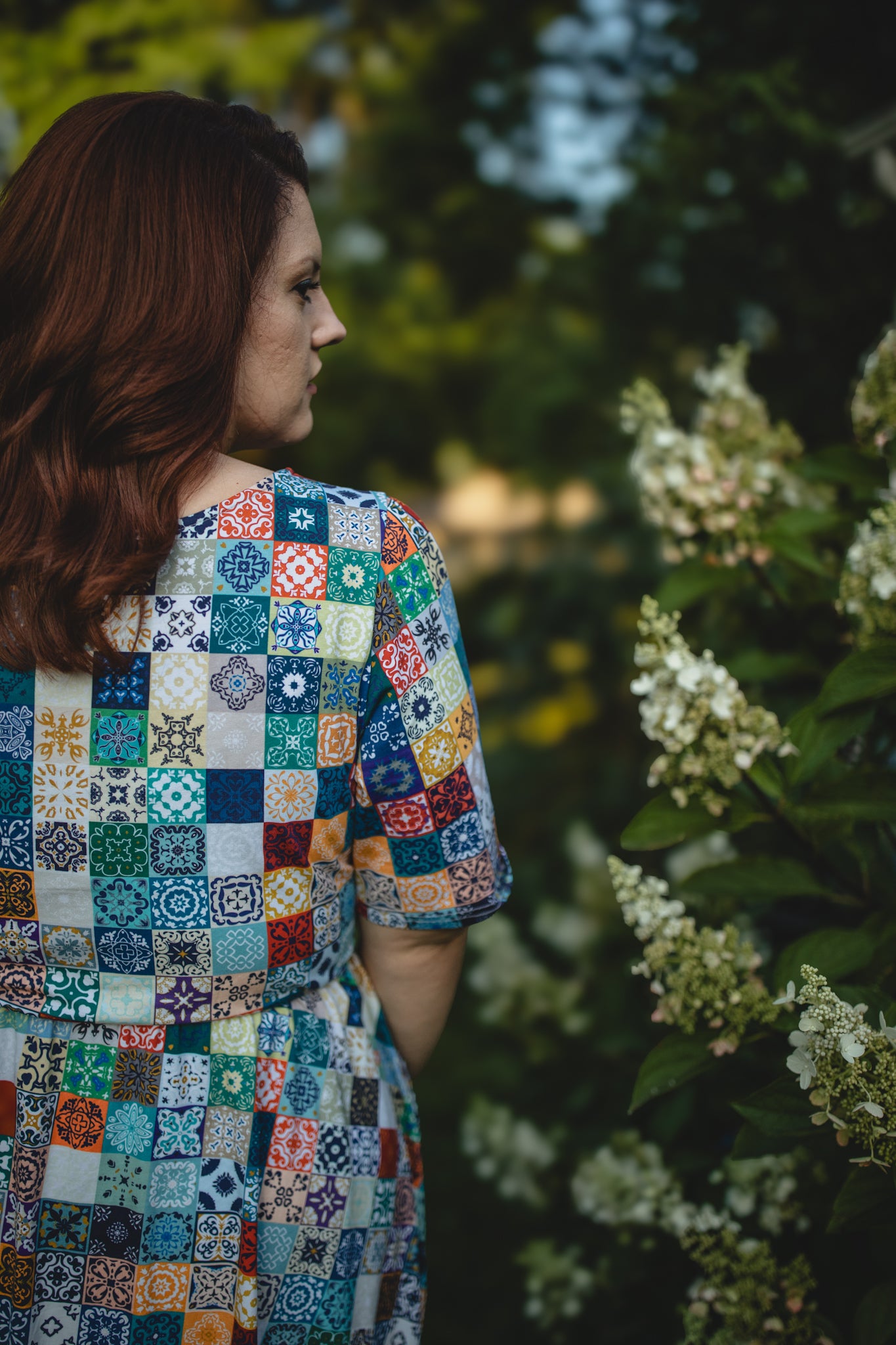 Woman wearing a colorful patterned modest nursing dress standing in a garden.