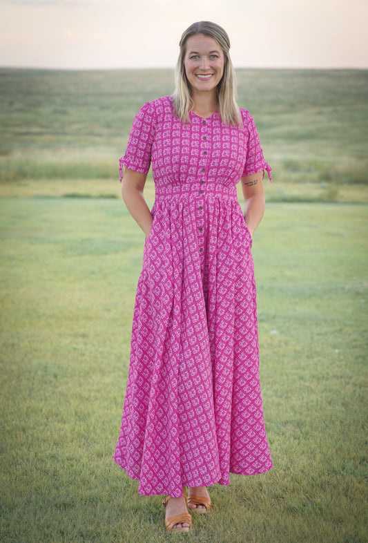 Woman wearing a pink patterned modest nursing dress standing in a grassy field