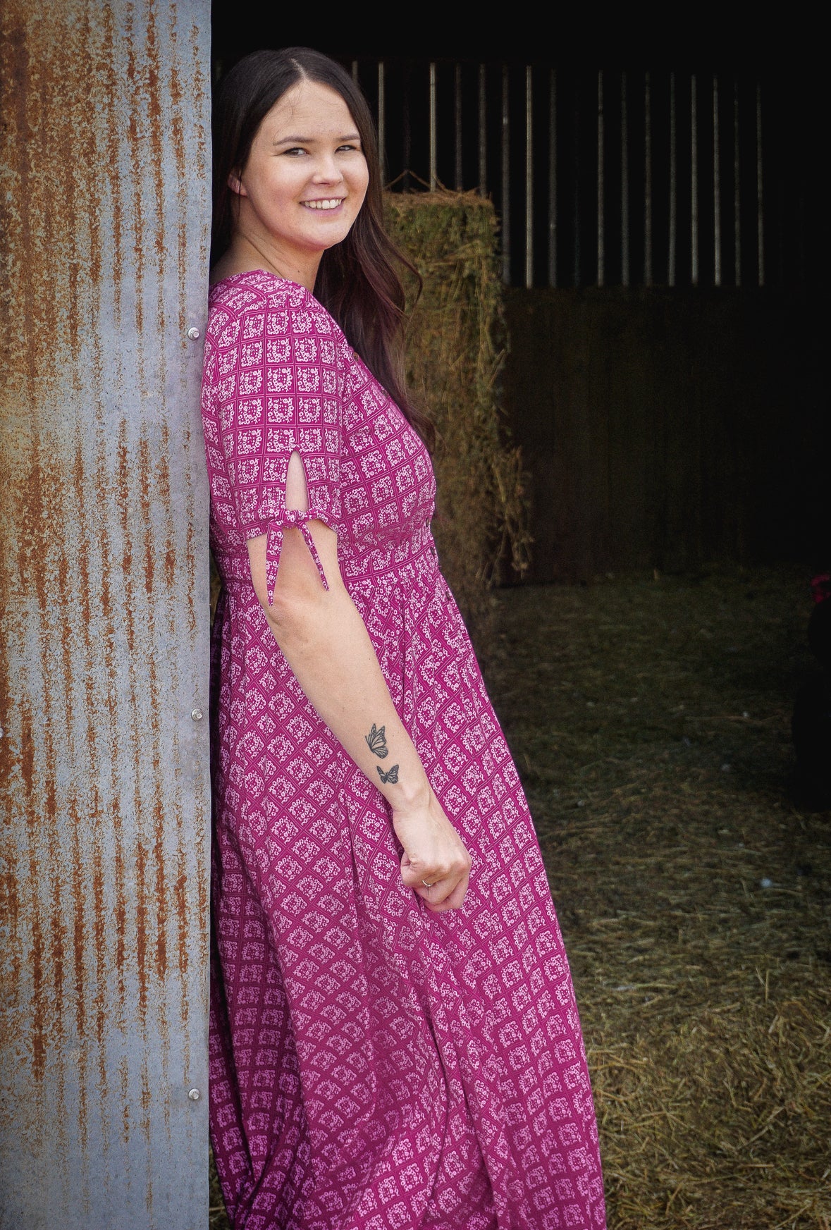 Woman in a pink modest nursing dress standing next to a rustic wall