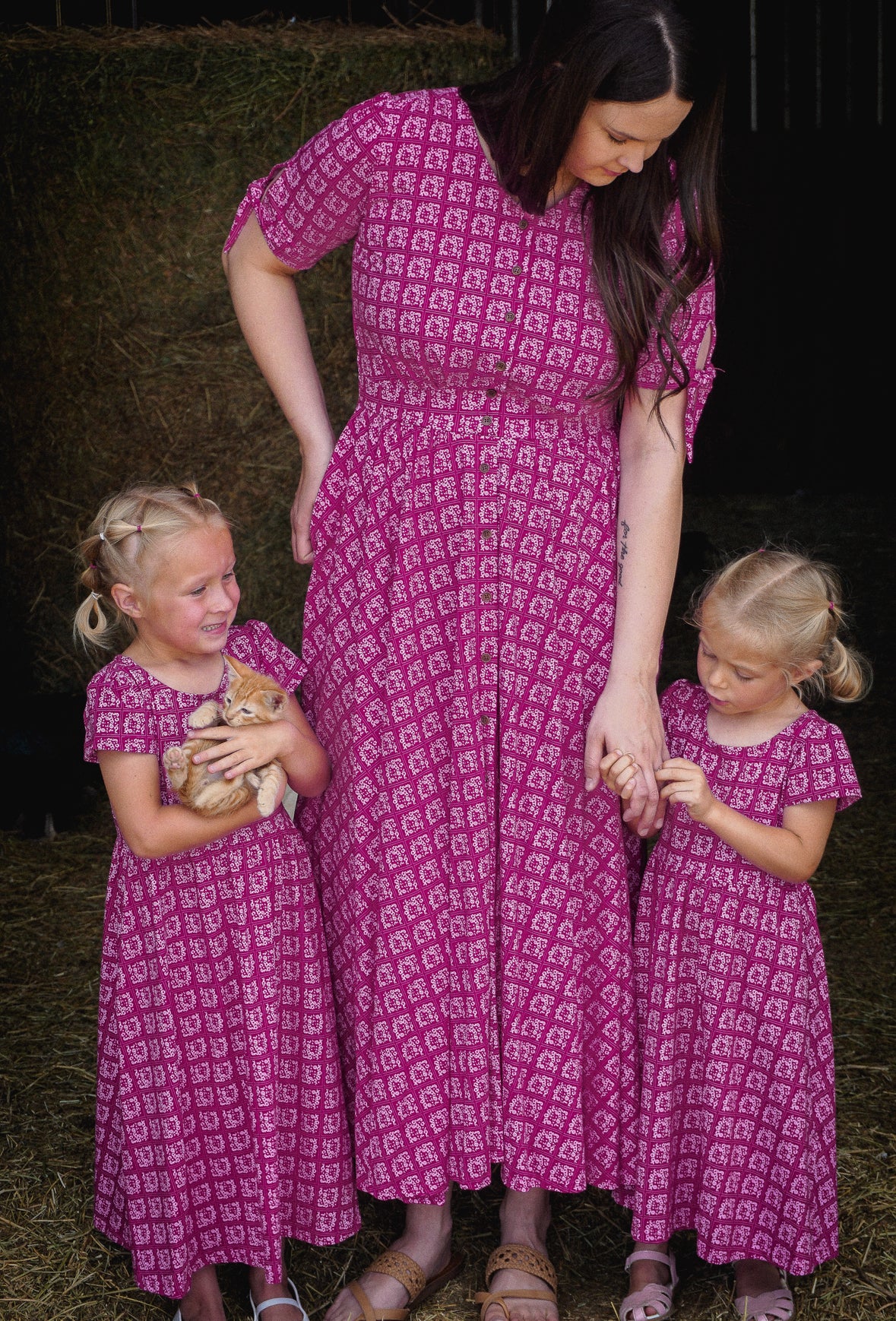 Woman and two young girls in matching pink modest dresses standing outdoors.