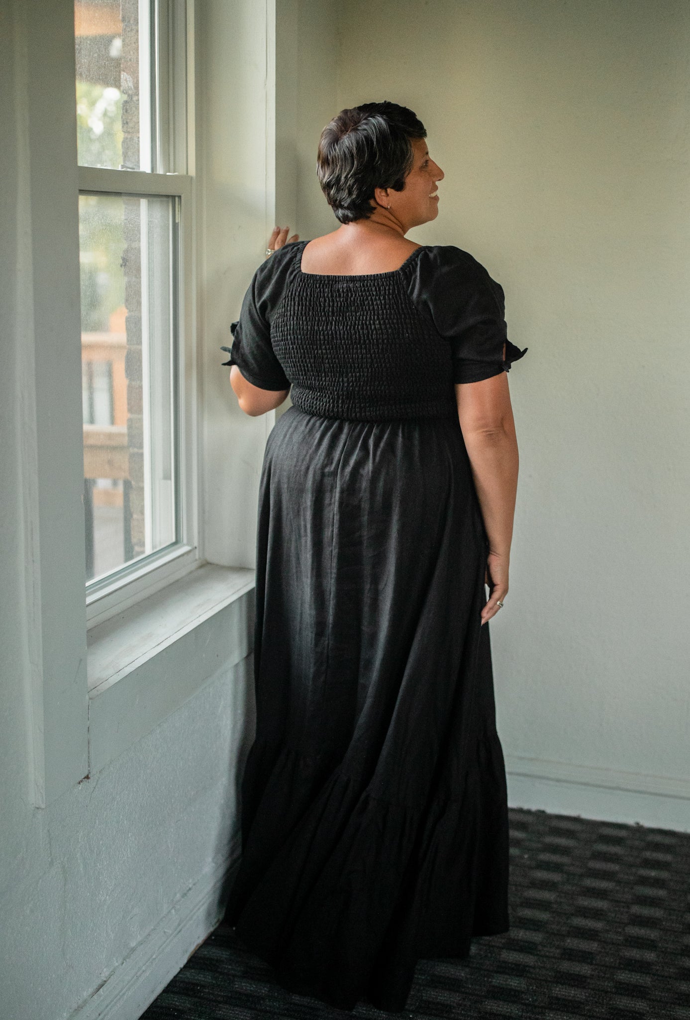 Woman in a long black modest nursing dress standing by a window