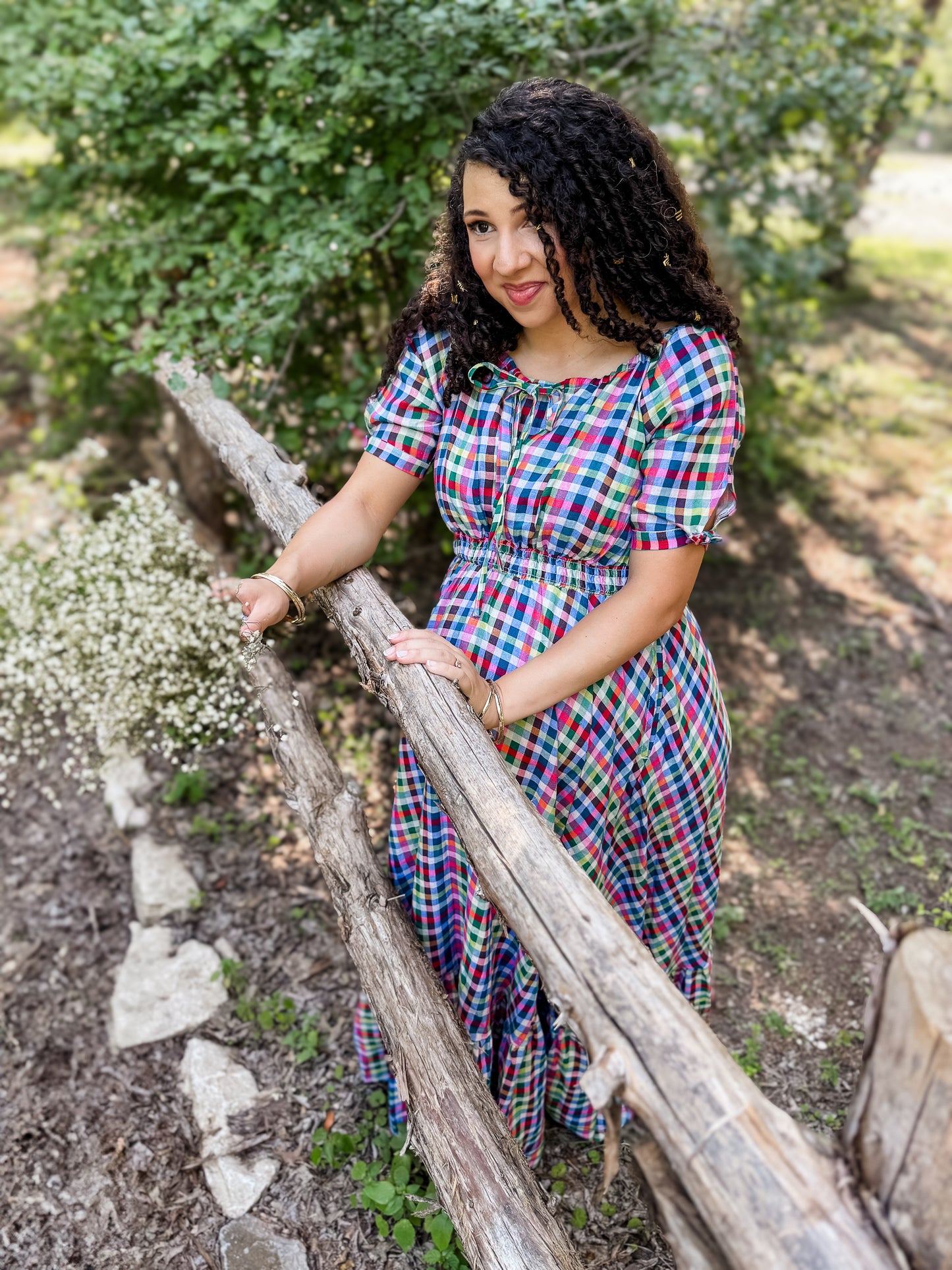 Woman in a colorful modest nursing dress standing outdoors near a wooden fence with greenery in the background