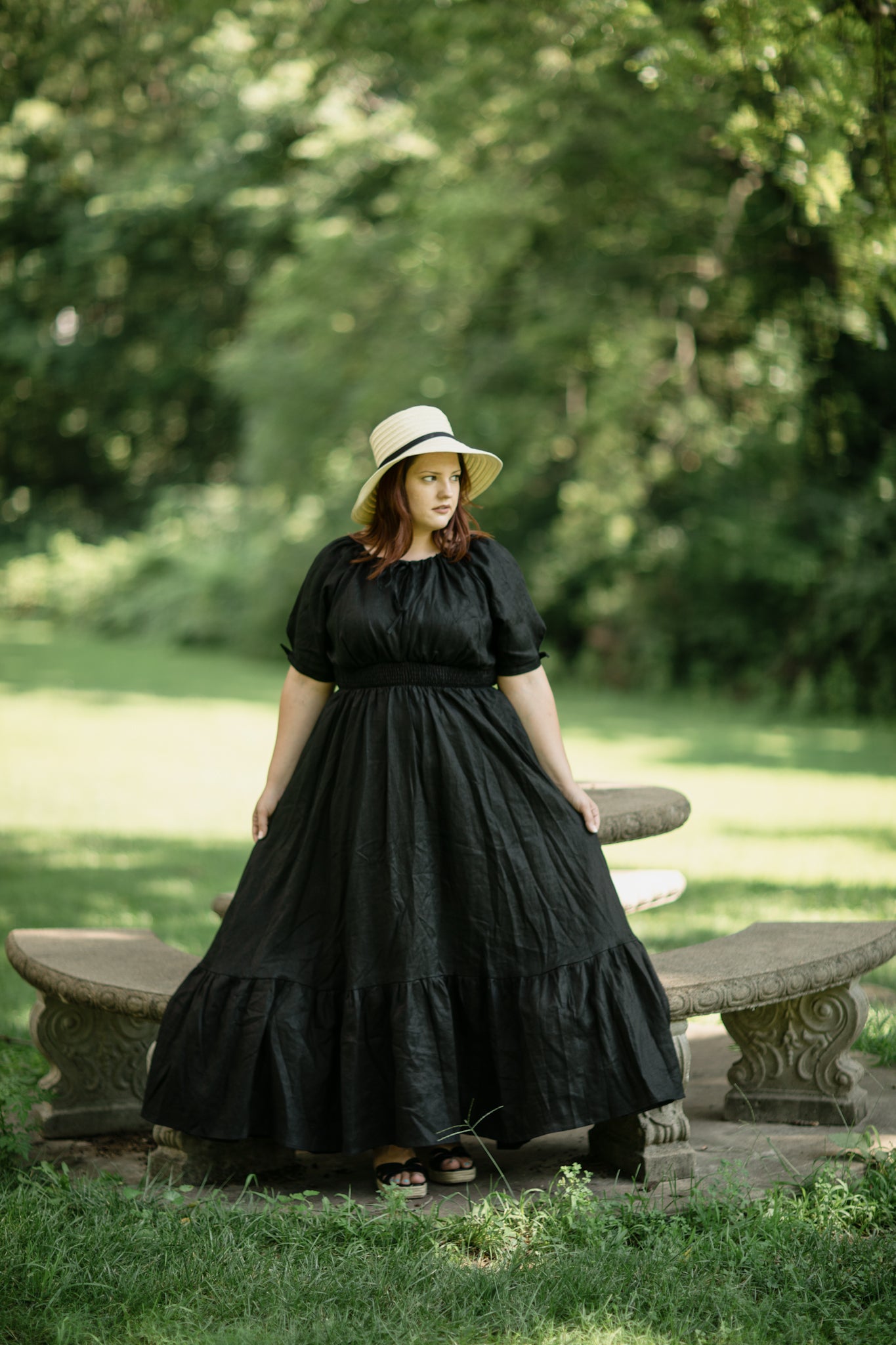 Woman in a black modest nursing dress and hat standing in a park